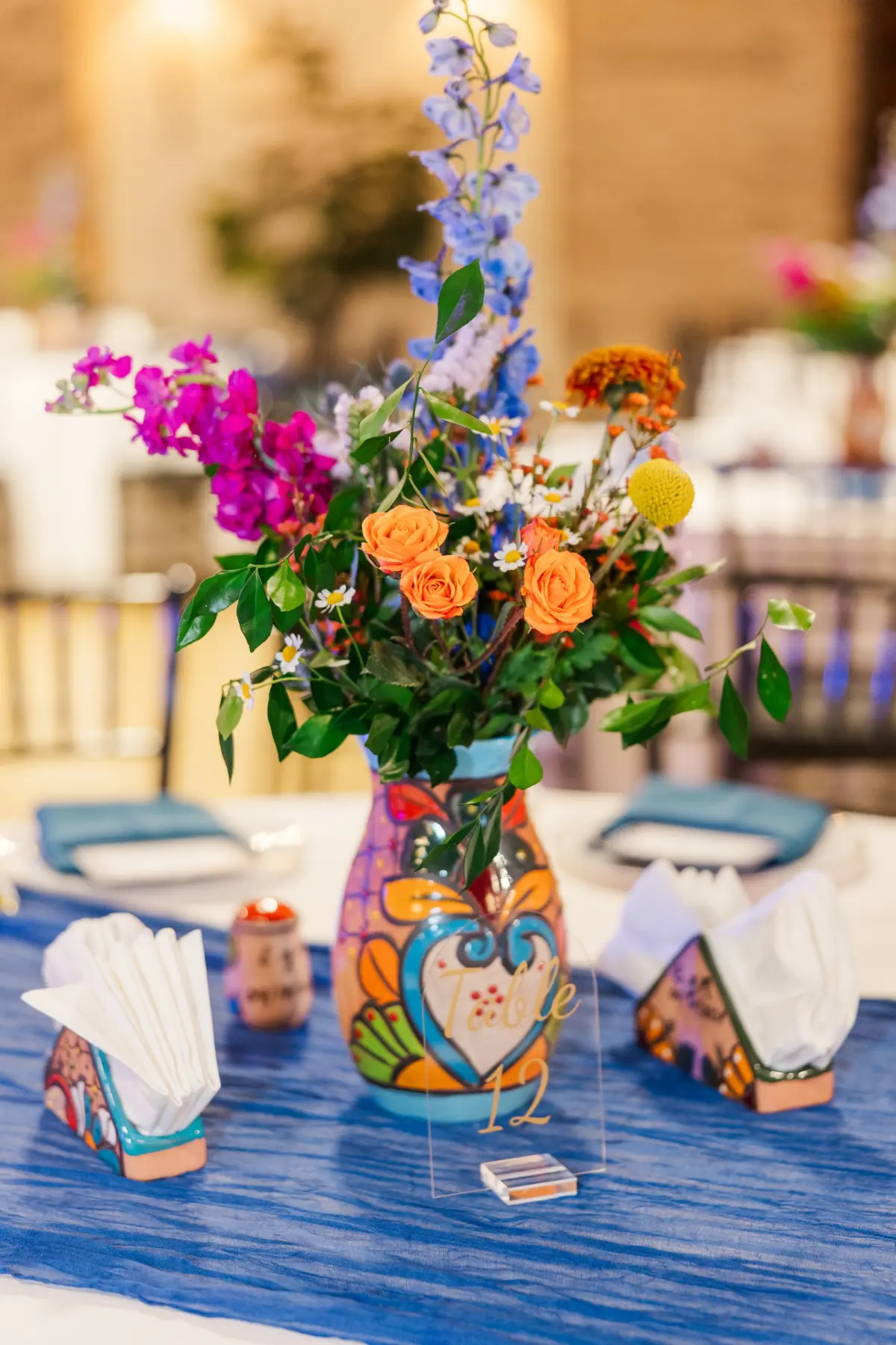 29Vibrant Blue Mexican Wedding Ideas - Blue Mexican-Inspired Winter Haven Wedding | Venue 650 Mexican Pottery Vase Wedding Reception Centerpiece with Tall Blue Delphiniums, Orange Rose, Purple and Pink Florals with Greenery Flower Arrangements Inspiration | Mexican Pottery Table Decor Ideas