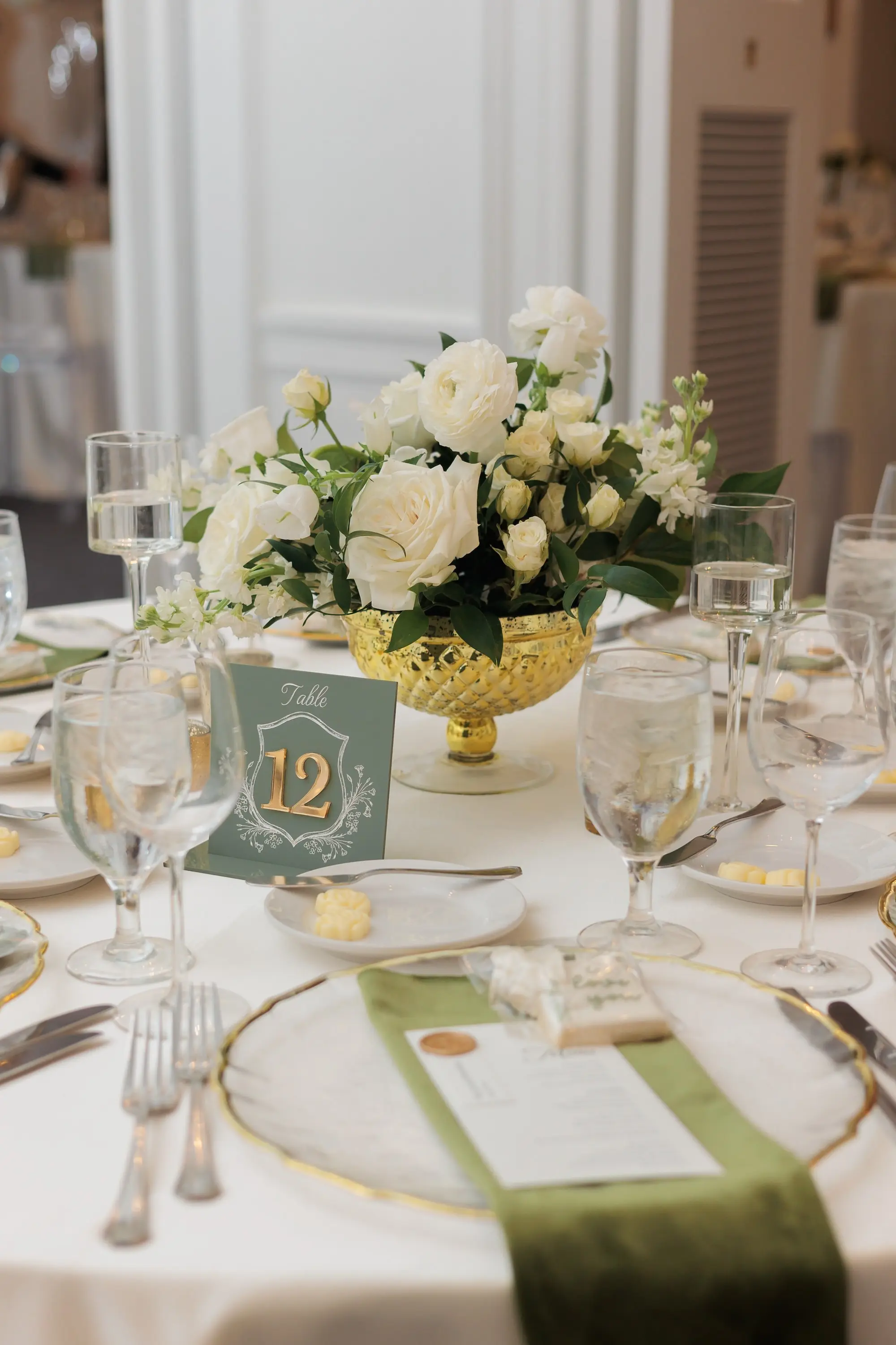 Timeless Ballroom Wedding Reception | Short Lush Centerpieces in Gold Bowl Vase with White Flower Arrangement Ideas | White Linens with Gold Rimmed Chargers and Olive Green Napkins Tablescape Decor Inspiration | Teal Green and Gold Wedding Reception Table Number Ideas | Tampa Bay Kate Ryan Event Rentals | Florist Save The Date Florida | Planner EventFull Weddings