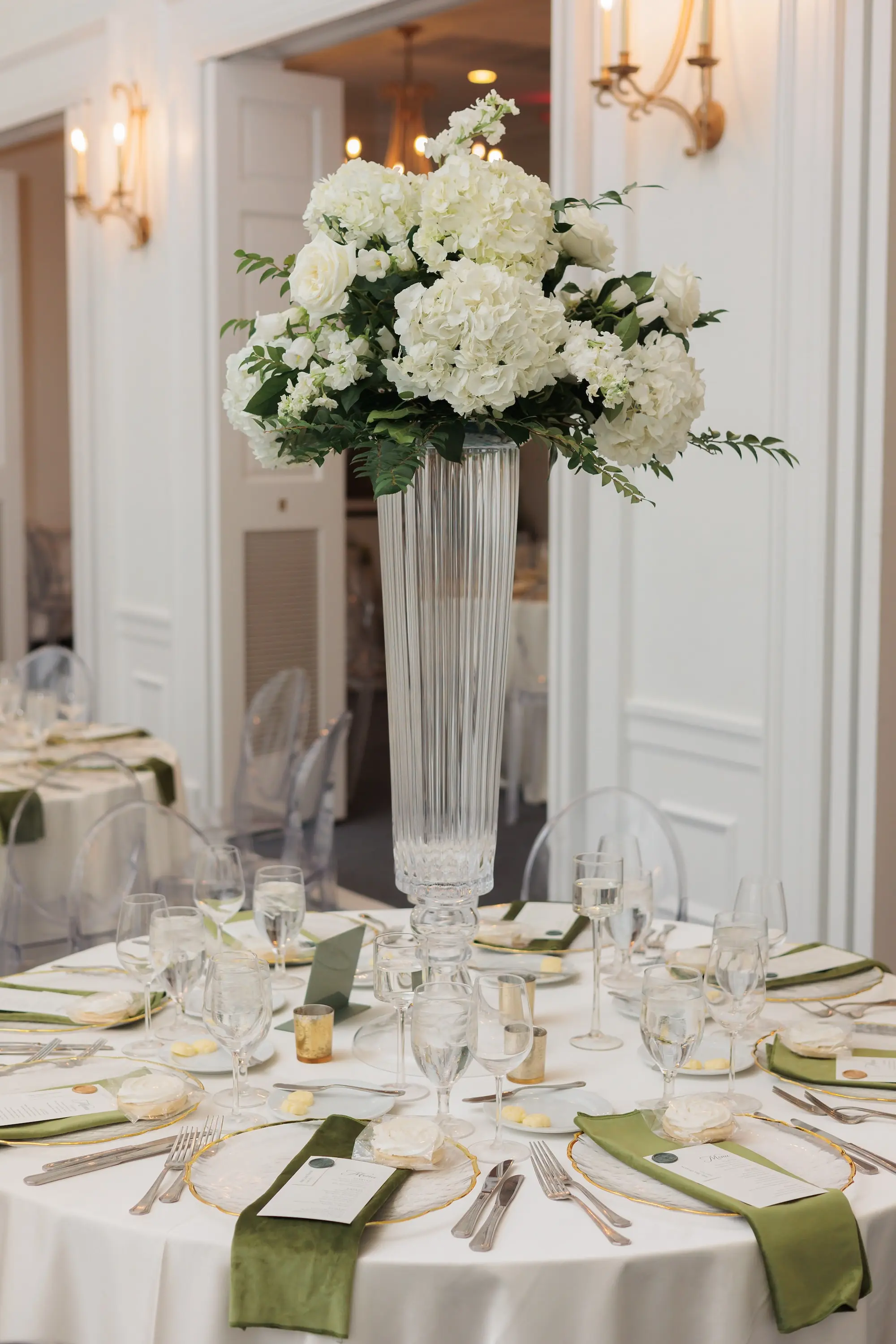 Timeless Ballroom Wedding Reception | Modern Clear Ghost Chairs | Tall Glass Centerpieces with White Hydrangeas, Roses, and Orchid Flower Arrangement Ideas | Greenery Eucalyptus Garland Decor Inspiration | White Linens with Gold Rimmed Chargers and Olive Green Napkins Romantic Candlelight Tablescape Decor Ideas | Tampa Bay Kate Ryan Event Rentals | Florist Save The Date Florida | Planner EventFull Weddings