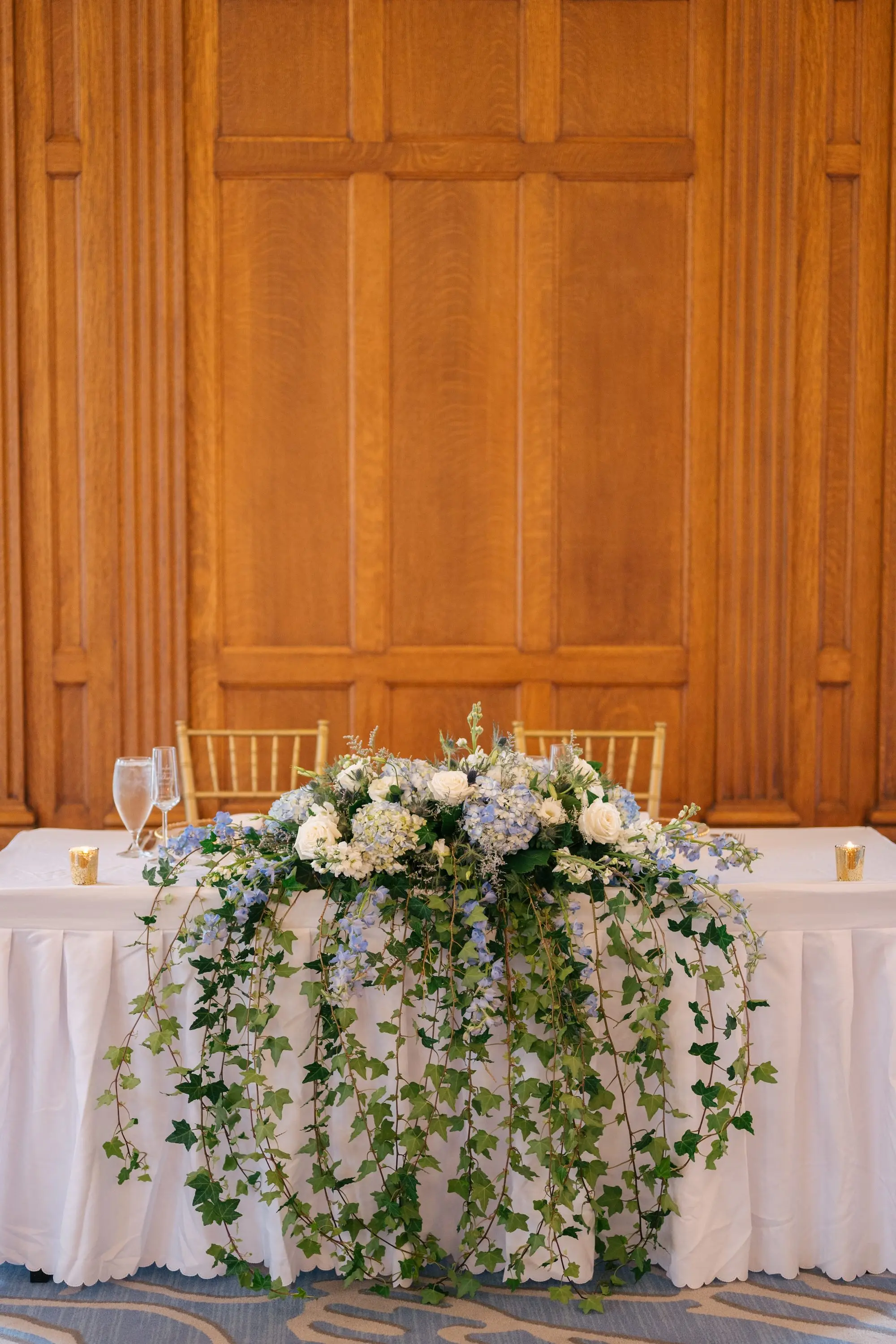 Romantic Long Sweetheart Table Wedding Reception with White and Light Blue Hydrangeas with Hanging Vines Inspiration | Gold Tea Candles on White Linens with Gold Chairs Ideas
