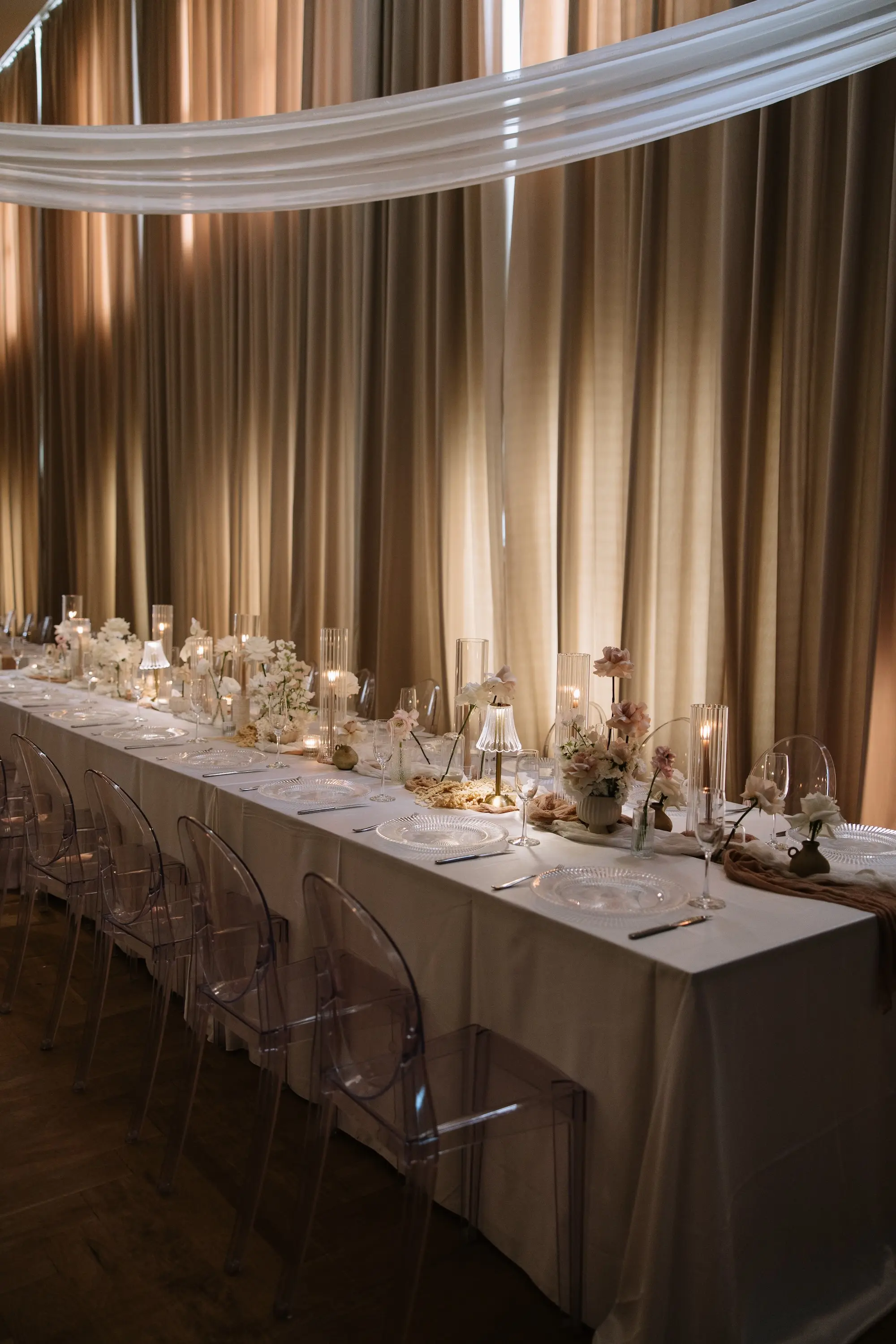Luxurious Ballroom Wedding Reception | Modern Clear Chairs and White Linens on Long Table Decor Inspiration | Single Stem Centerpieces in Bud Vases with White Flower Arrangement Ideas | Romantic Taper Candles in Vases and Small Gold Table Lamps Decor Inspiration | White Linen Ceiling and Wall Draping Ideas | Tampa Bay Planner EventFull Weddings | Ybor Event Venue Hotel Haya