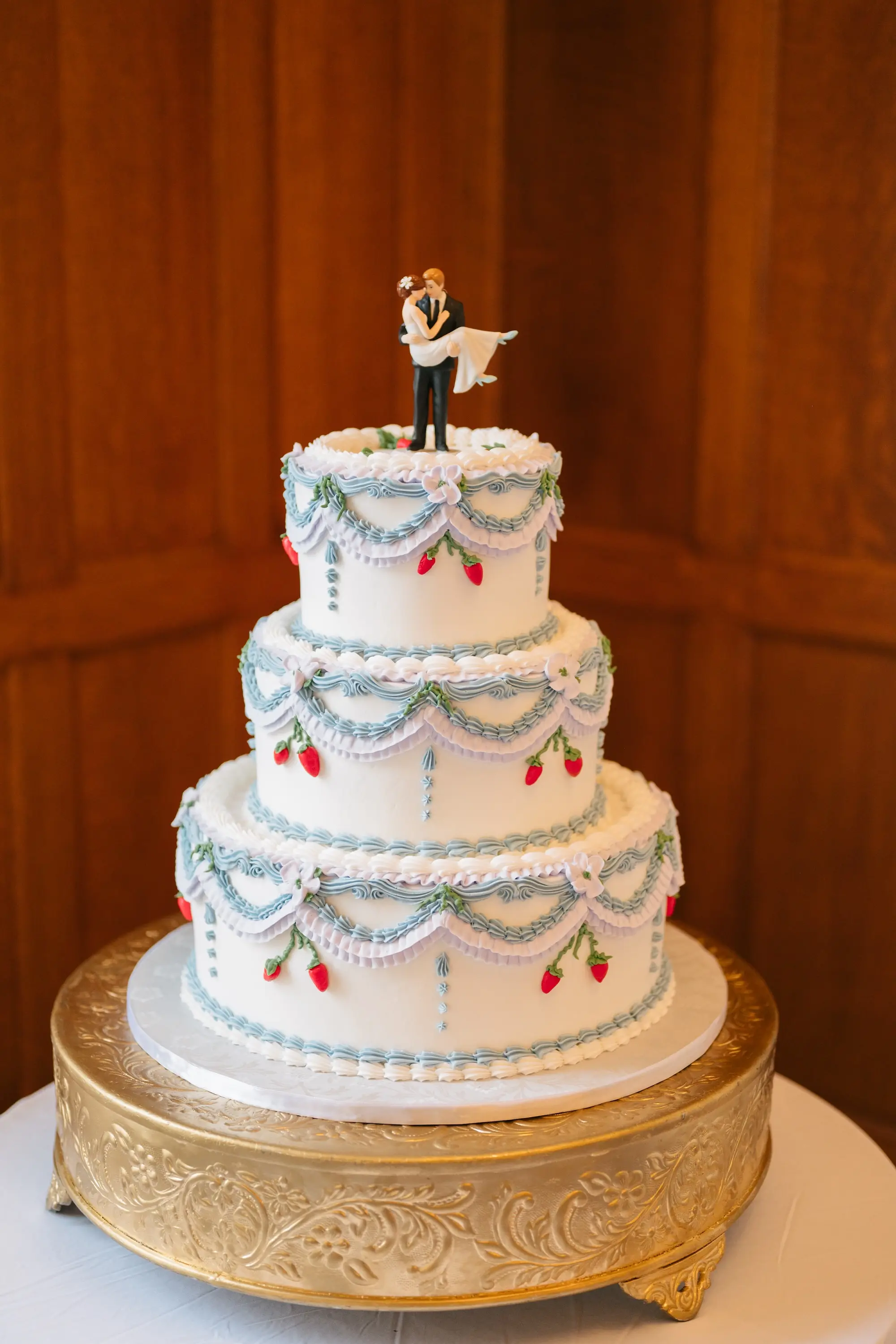 Three Tier Wedding Cake with Strawberry Details and White and Blue Icing Details Inspiration | Groom Holding Bride Wedding Cake Topper Ideas