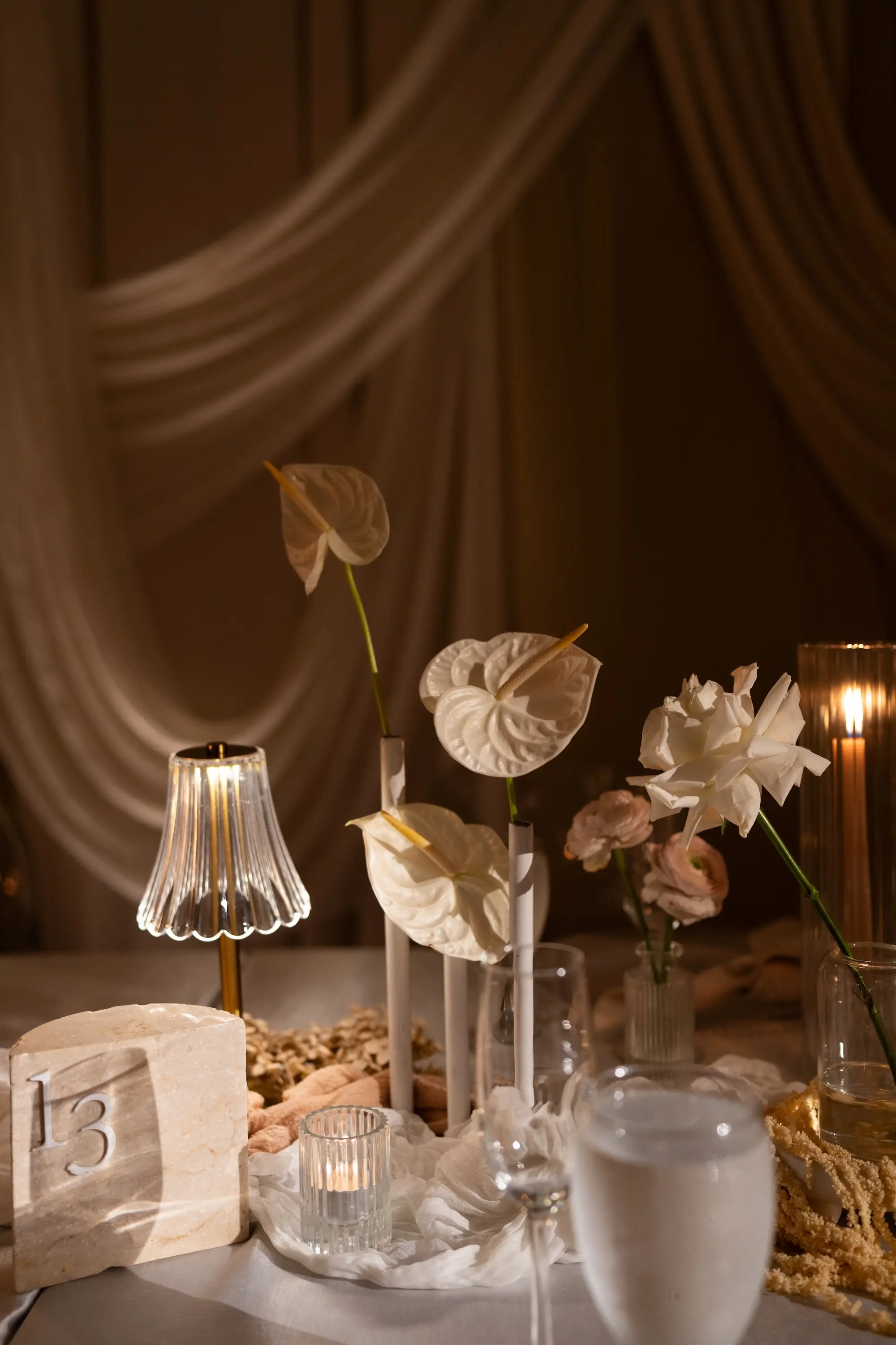 Soft, Romantic Ballroom Wedding Reception Tablescape Inspiration | Ethereal Candlelight Decor Ideas | Single Stem Anthuriums and Roses Florals in Glass Bud Vase Wedding Reception Table Decor Inspiration | White, Cream, and Soft Gold Wedding Reception Decor Ideas | White Linens with Candles and Small Decorative Table Lamps Inspiration | Stone Quartz Table Number Ideas | Tampa Bay Planner EventFull Weddings