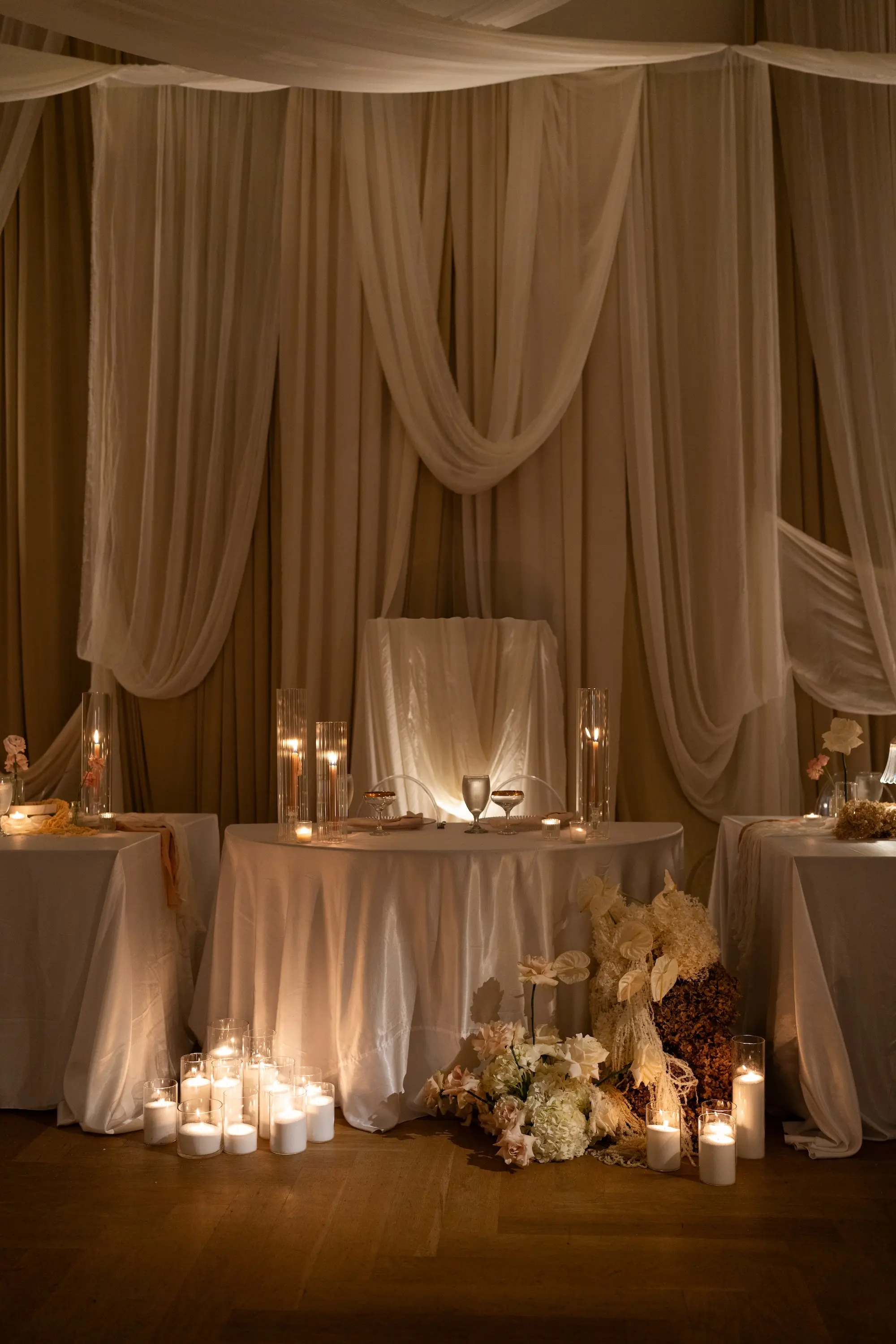 Luxurious Ballroom Wedding Reception Sweetheart Table Inspiration | White Linen Tablecloth with Romantic Taper Candles and Champagne Coupes Ideas | Ethereal Wall Draping Fabric and Large Candles in Clear Vases Decor Inspiration | Neutral Flower Arrangement Decor with White, Blush, Brown Hydrangeas, Carnations and Roses Ideas | Tampa Bay Planner EventFull Weddings