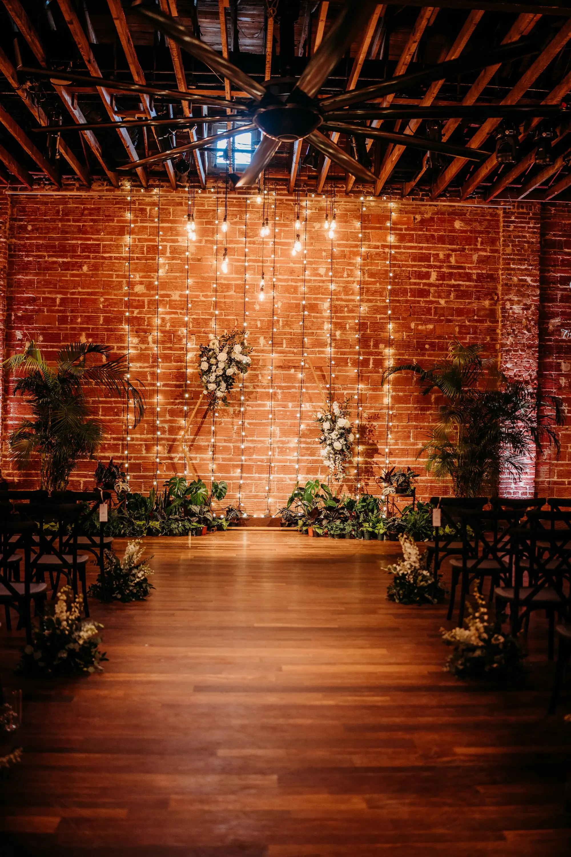 Moody, Romantic Wedding Ceremony Wedding Decor with Green Palms and White Florals Inspiration | String Light Backdrop on Exposed Brick Wall Ideas | Modern, Industrial Wedding Venue Inspiration | Tampa Bay Premier Wedding Venue NOVA 535 in Downtown St. Pete