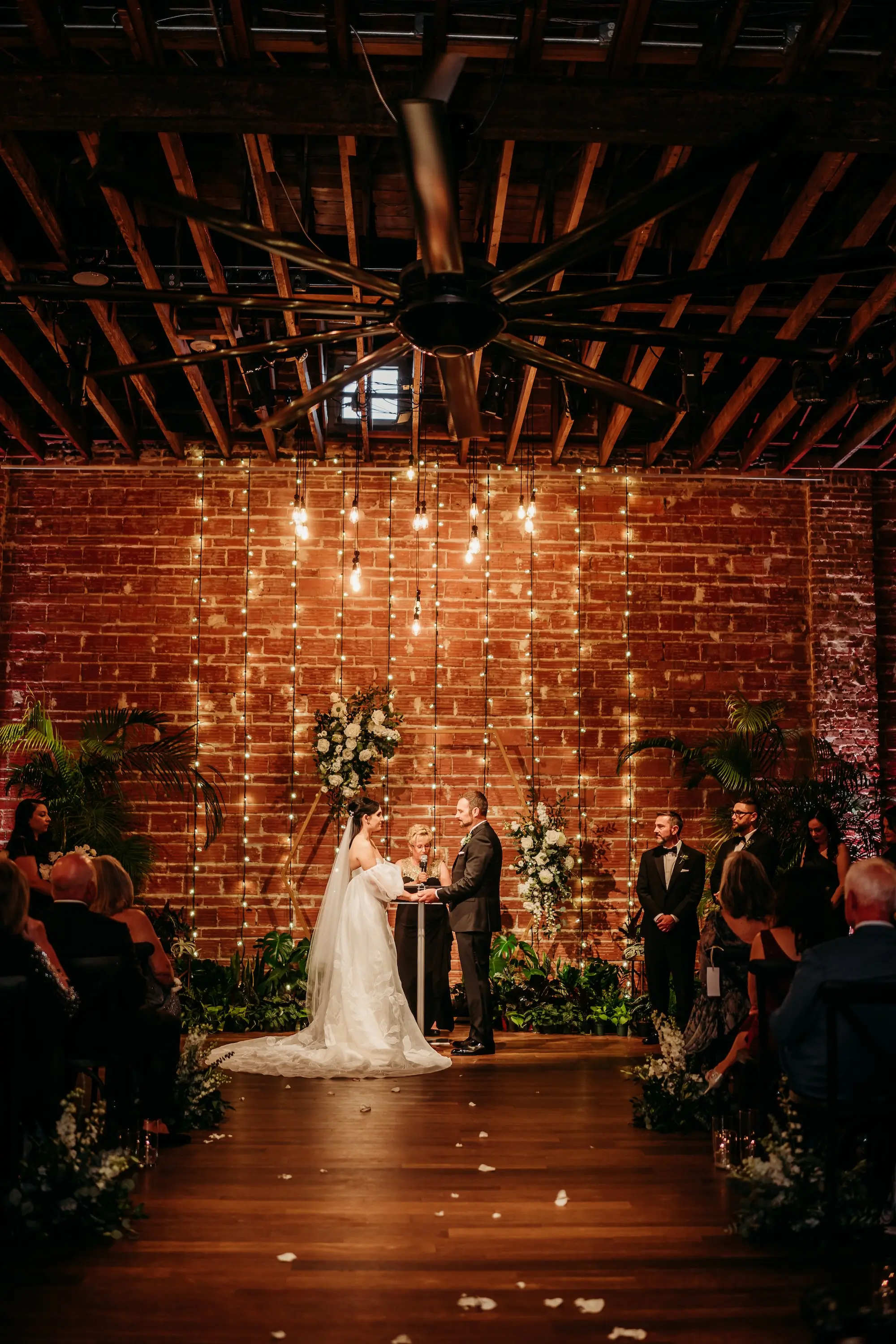 Bride and Groom Wedding Ceremony Vow Exchange Wedding | Moody, Romantic Wedding Ceremony Wedding Decor with Green Palms and White Florals Inspiration | String Light Backdrop on Exposed Brick Wall Ideas | Modern, Industrial Wedding Venue Inspiration | Premier Wedding Venue NOVA 535 in Downtown St. Pete | Tampa Bay Photographer Sabrina Autumn Photography