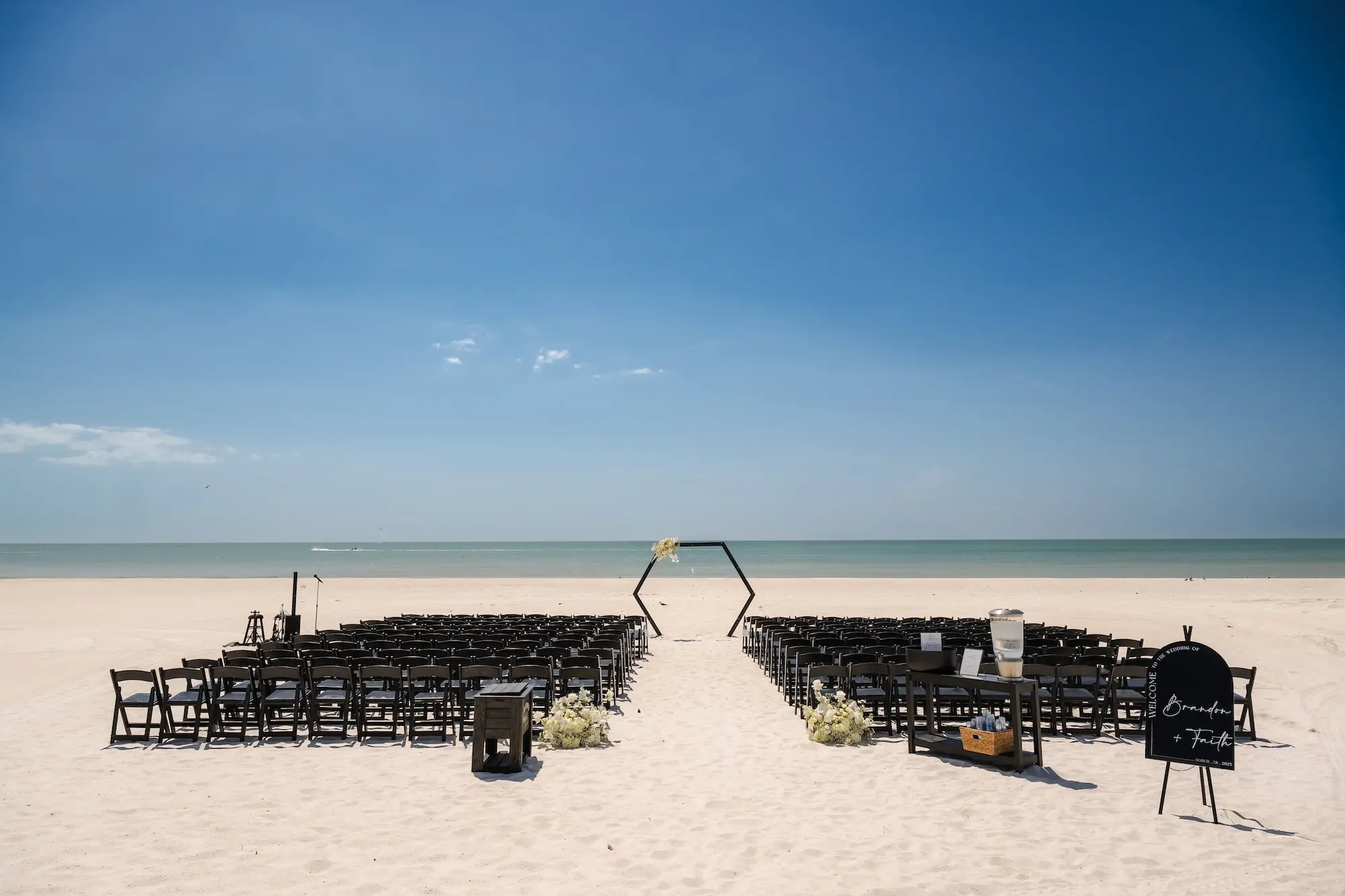Classic Champagne and Black Florida Beachfront Wedding Ceremony Decor Inspiration | Black Wooden Ceremony Chairs Ideas | White Roses and Baby's Breath Flower Arrangement Ceremony Aisle Decor Ideas | Beach Wedding Decor Inspiration | Black Hexagon Altar Backdrop Decor Ideas | Tampa Bay Event Venue Tradewinds Island Resort