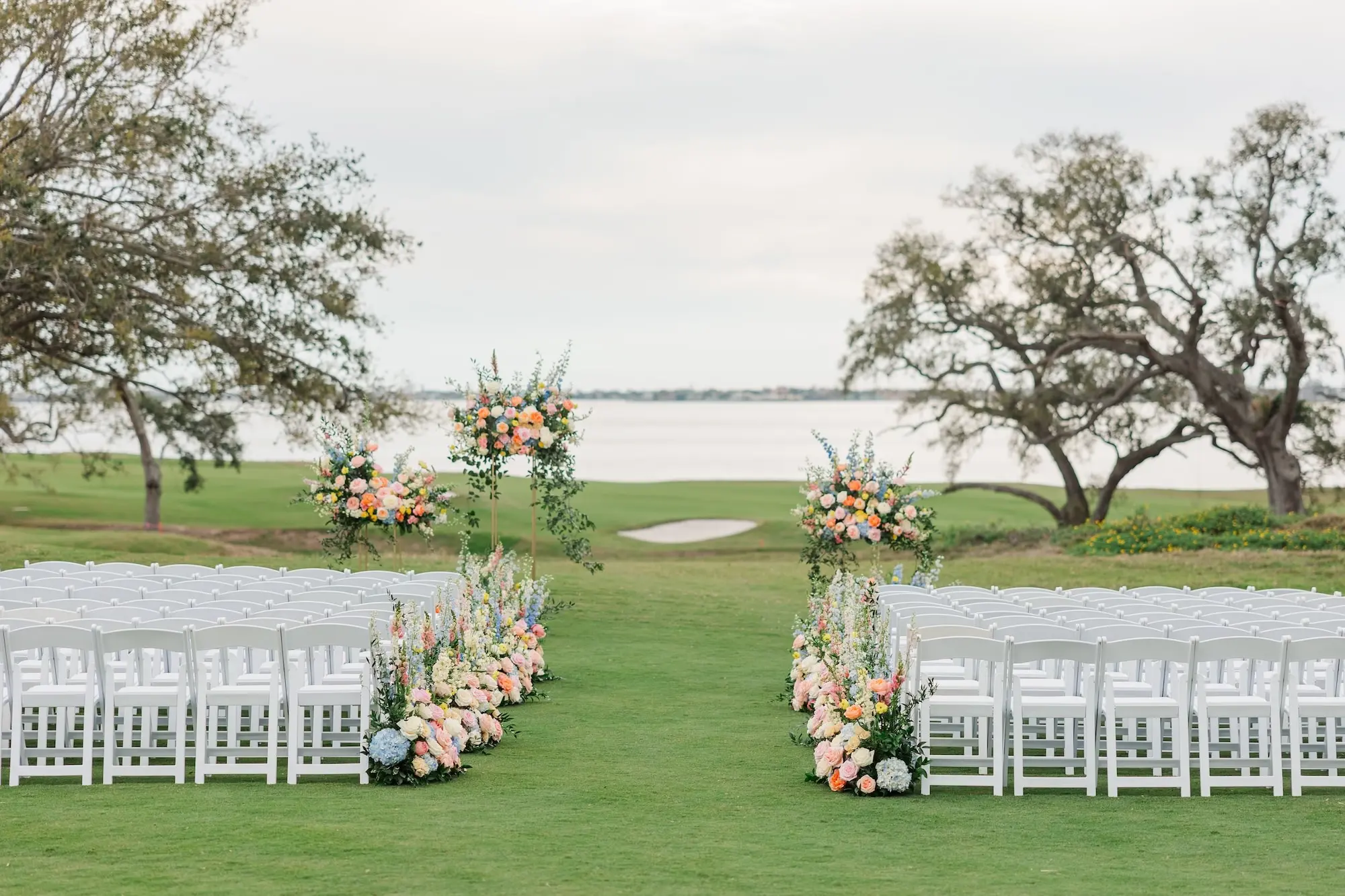 Spring Outdoor Garden Party Wedding Ceremony Decor Inspiration | Pastel Pink, Blue, Yellow, White, and Orange Hydrangeas, Peonies, Wisteria, Roses Flower Arrangement Ceremony Aisle Decor Inspiration | Country Club Golf Course Lawn Ceremony Ideas | Waterfront Wedding Venue Inspiration | White Ceremony Chairs Ideas | Clearwater Event Planner Parties A La Carte | Tampa Bay Venue Belleair Country Club | Florist Bruce Wayne Florals