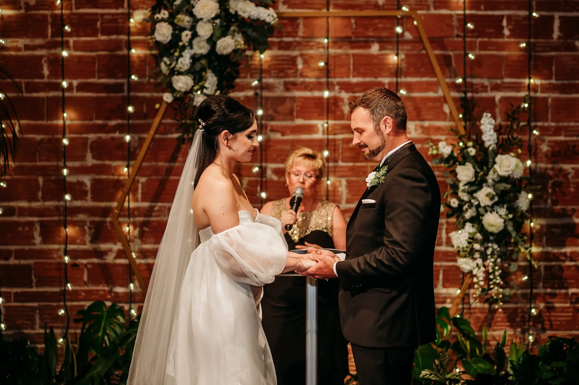Bride and Groom Wedding Ceremony Vow Exchange Wedding | Moody, Romantic Wedding Ceremony Wedding Decor with Green Palms and White Florals Inspiration | String Light Backdrop on Exposed Brick Wall Ideas | Modern, Industrial Wedding Venue Inspiration | Premier Wedding Venue NOVA 535 in Downtown St. Pete | Tampa Bay Photographer Sabrina Autumn Photography