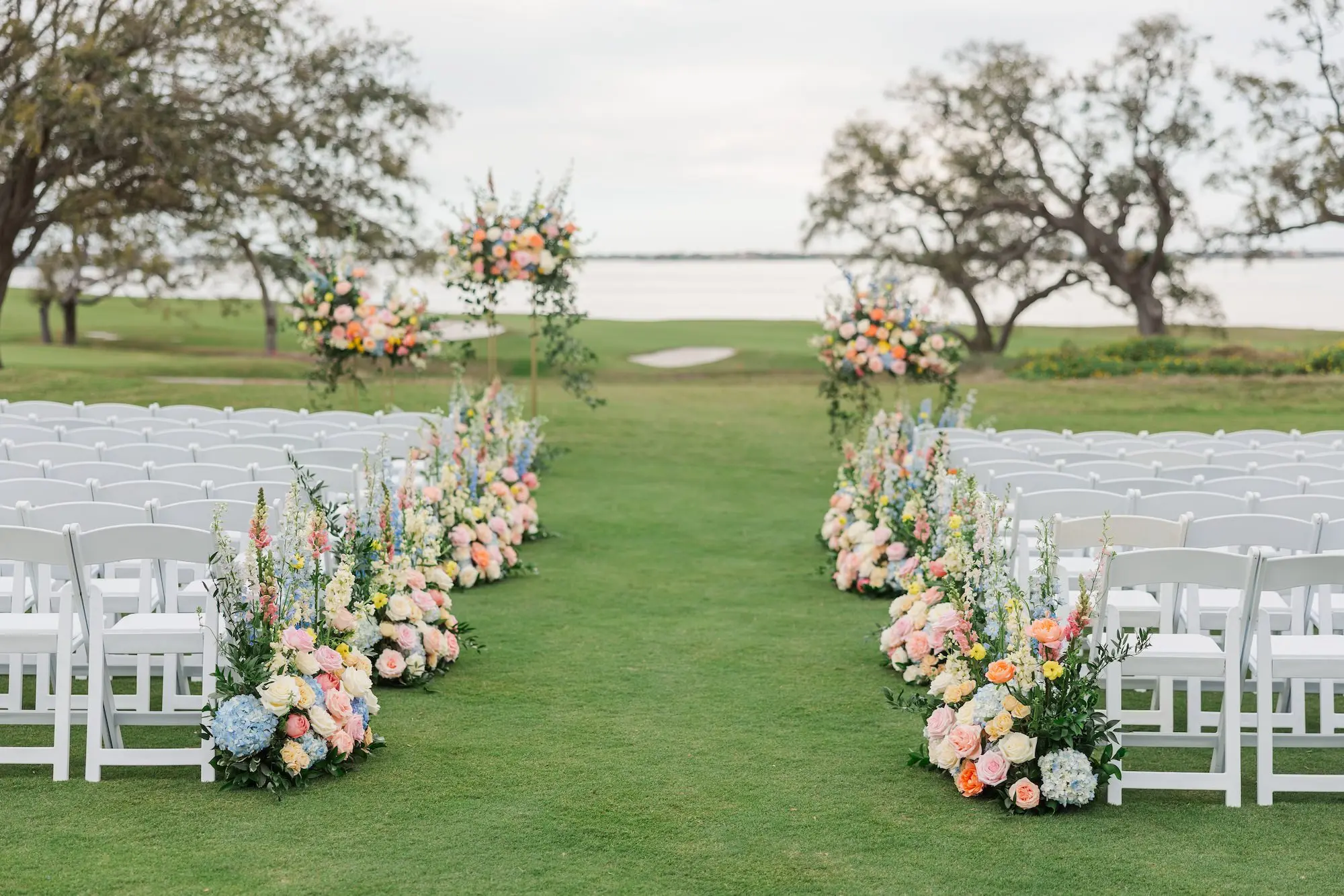 Spring Outdoor Garden Party Wedding Ceremony Decor Inspiration | Pastel Pink, Blue, Yellow, White, and Orange Hydrangeas, Peonies, Wisteria, Roses Flower Arrangement Ceremony Aisle Decor Inspiration | Country Club Golf Course Lawn Ceremony Ideas | Waterfront Wedding Venue Inspiration | White Ceremony Chairs Ideas | Clearwater Event Planner Parties A La Carte | Tampa Bay Venue Belleair Country Club | Florist Bruce Wayne Florals
