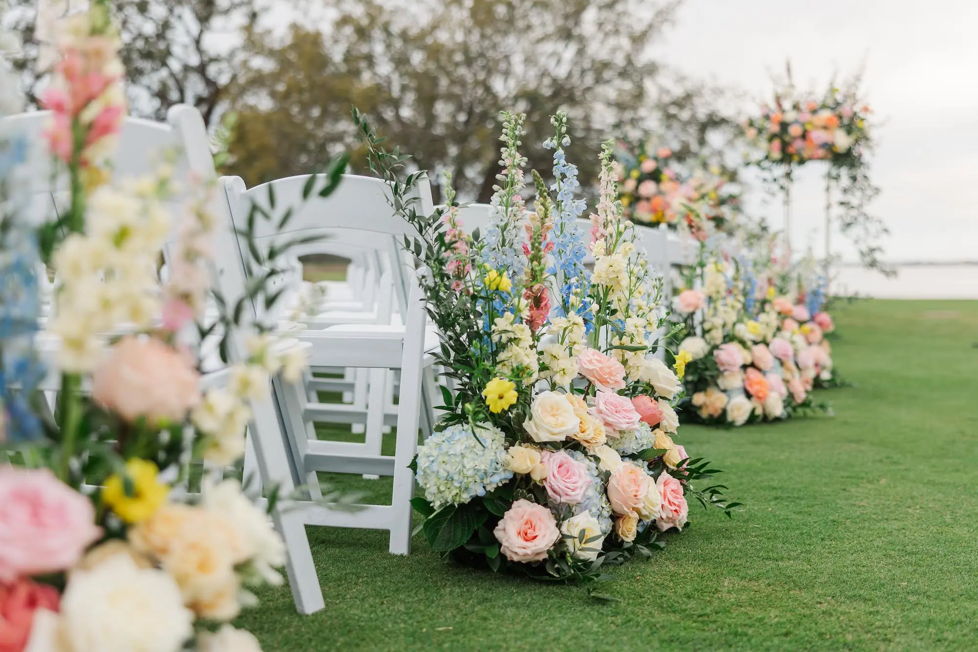 Bridgerton Spring Outdoor Garden Party Wedding Ceremony Aisle Decor Ideas | Pastel Blue, Pink, White, Yellow, and Orange Flower Arrangement Inspiration | White Ceremony Chair Ideas | Clearwater Florist Bruce Wayne Florals