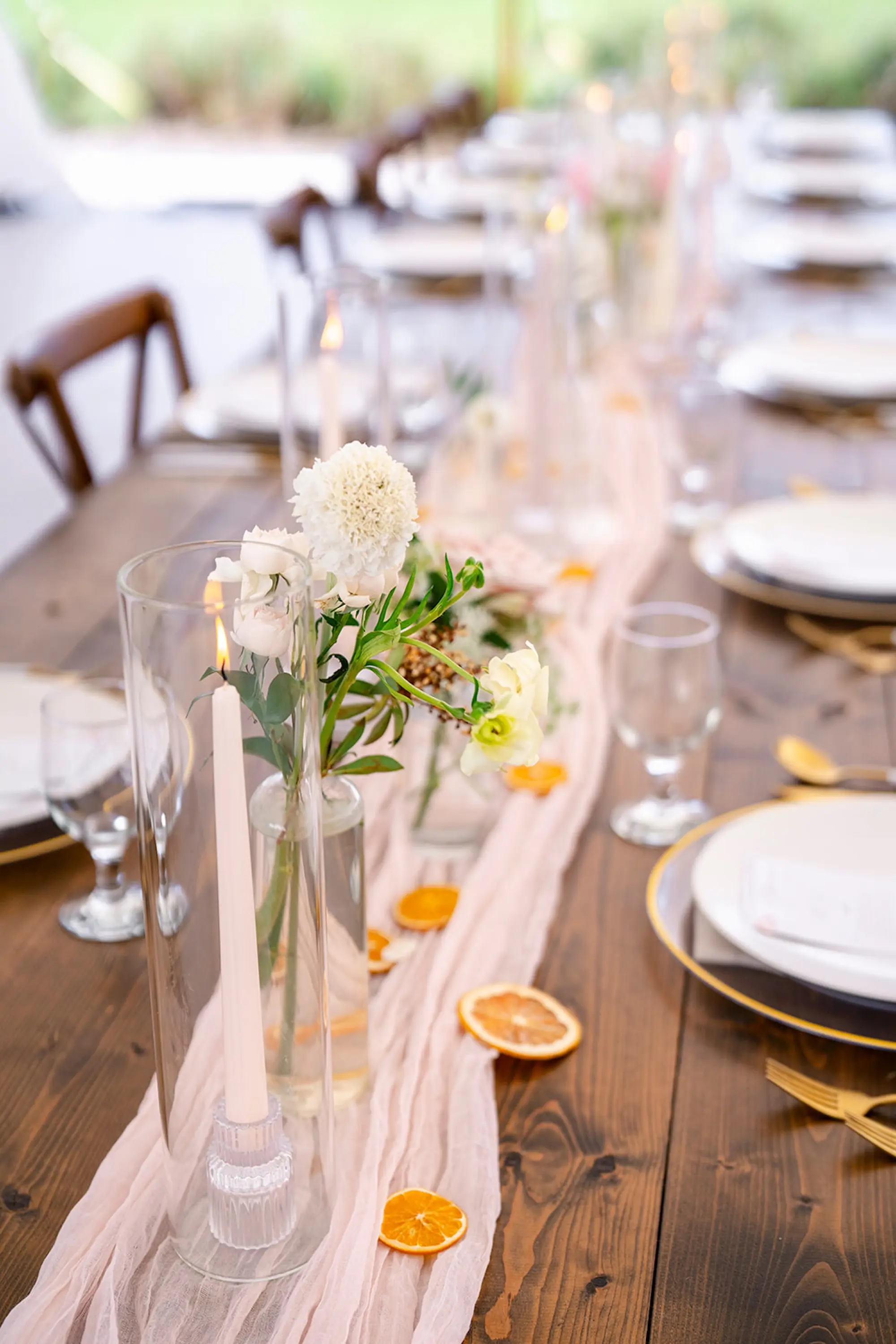 Elegant White and Gold Wedding Reception Place Setting Decor Inspiration | Clear Chargers with Gold Rim and Gold and White Flatware Tablescape Decor Ideas | Light Pink Chiffon Garland with Lush White and Light Pink Floral Arrangements with Citrus Oranges and White Taper Candles Centerpiece Decor Inspiration | Tampa Bay Planner Wilder Mind Events