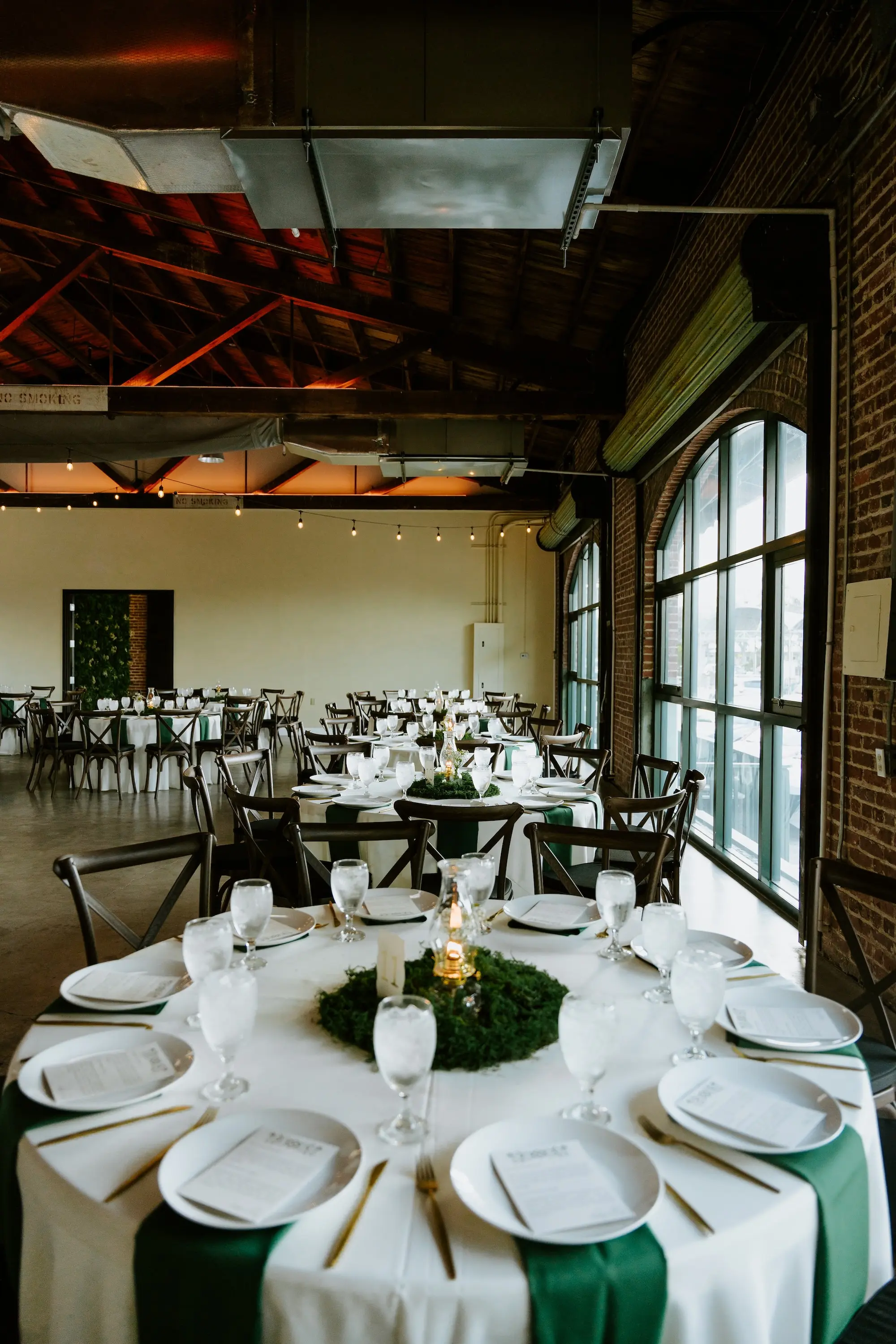 Modern Industrial Rustic Exposed Brick Ballroom Wedding Reception | Rustic Wooden Chairs at Round Tables with White Table Linens and Dark Green Napkins | Short Simple Romantic Moss Centerpieces with Candlelight Ideas | Whimsical Woodland Fantasy Wedding Theme Inspiration | Venue St. Petersburg Venue Morean Center for Clay