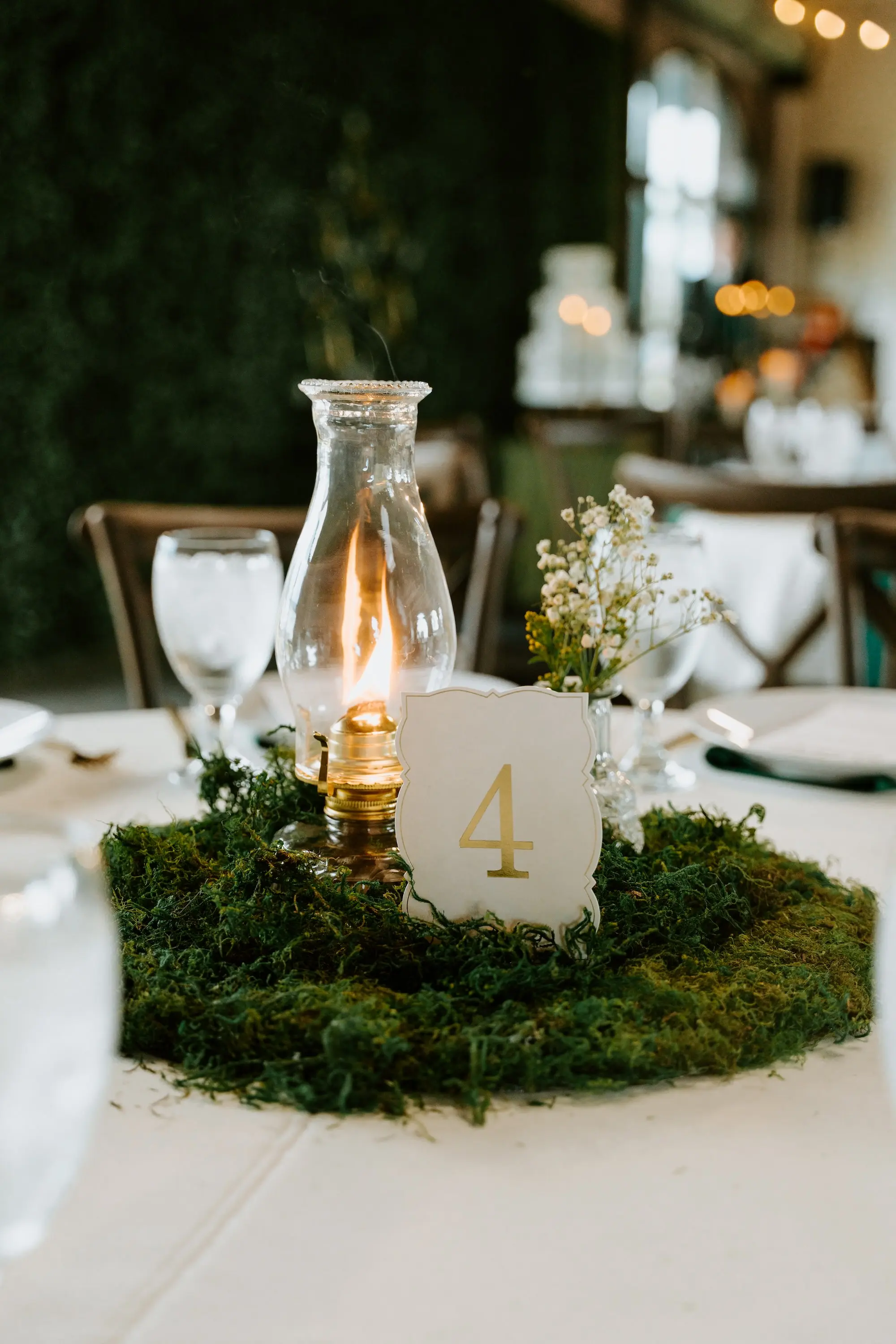 Woodland Fantasy Wedding Reception Centerpieces with Moss, Baby's Breath in Bud Vase and Oil Lamp Candle Decor Ideas | White and Gold Cardstock Table Numbers with Gold Numbers Inspiration | Magical Ethereal Wedding Theme Ideas