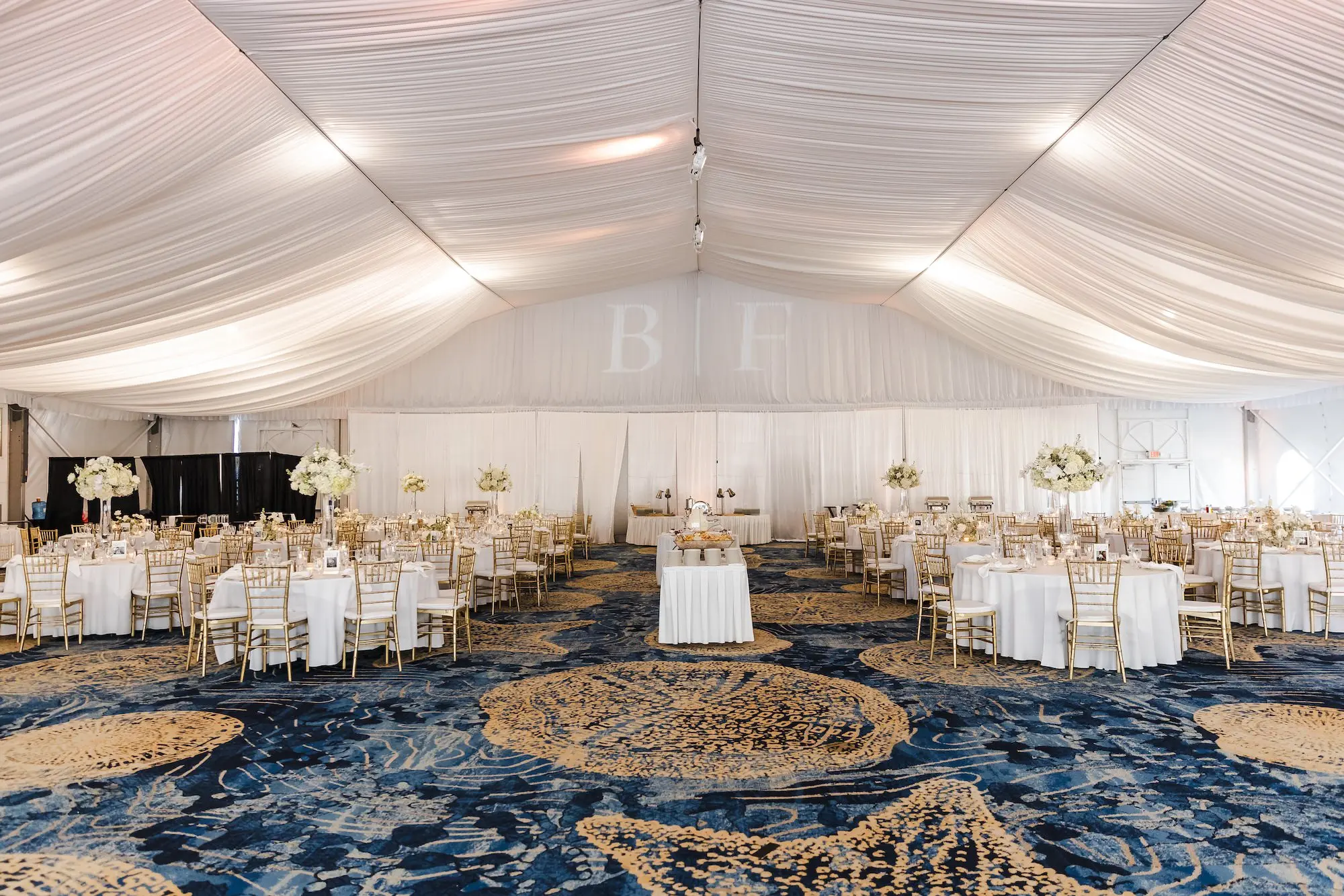Classic Champagne and Black Florida Beach Tented Ballroom Wedding Reception | White Flower Roses and Baby's Breath in Tall Glass Vase Centerpiece Decor Ideas | Projection Bride and Groom First Name Letters Inspiration | St Pete Beach Event Venue TradeWinds Island Resort