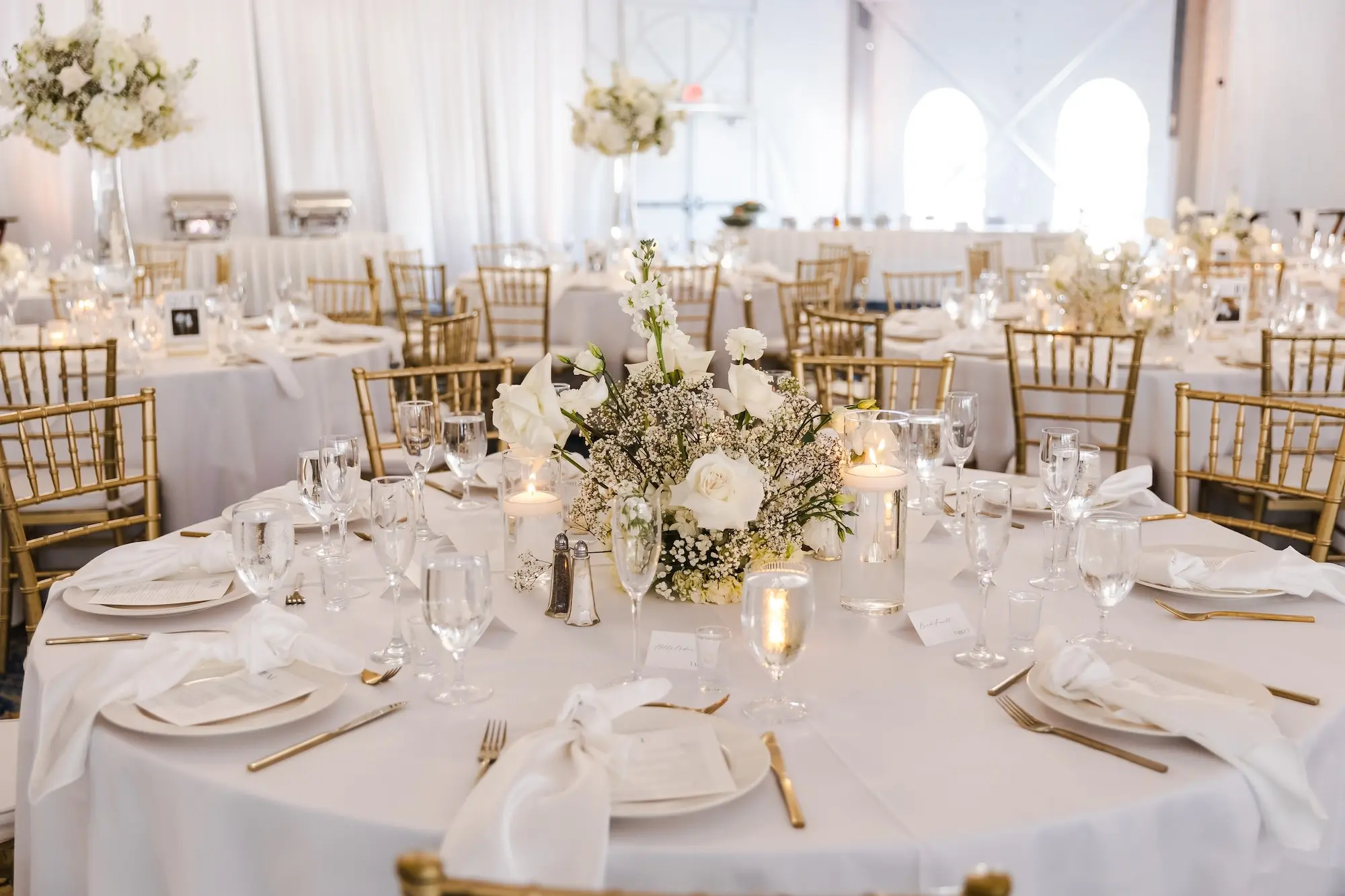 Classic Champagne and Black Florida Beach Tented Ballroom Wedding Reception | White Flower Roses and Baby's Breath Centerpiece Decor Ideas | Gold Chiavari Chairs at Round Tables with White Linens and Gold Flatware Tablescape Decor Inspiration
