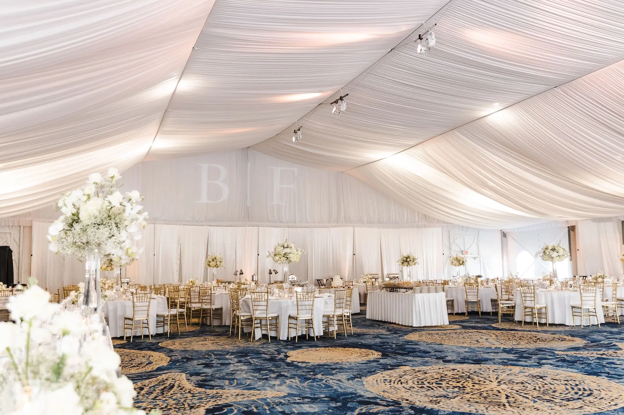 Classic Champagne and Black Florida Beach Tented Ballroom Wedding Reception | White Flower Roses and Baby's Breath in Tall Glass Vase Centerpiece Decor Ideas | Projection Bride and Groom First Name Letters Inspiration | St Pete Beach Event Venue TradeWinds Island Resort