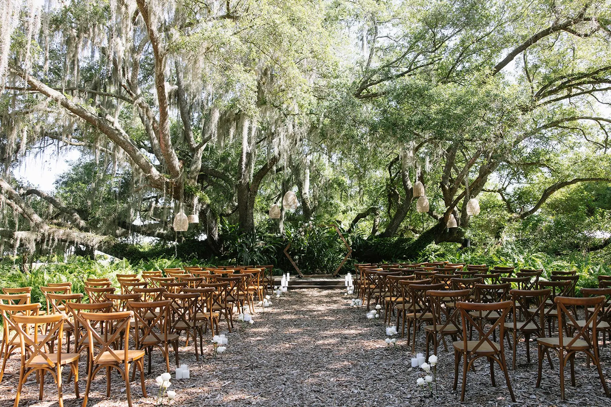 Romantic Lush Green Outdoor The Broken Oak Outdoor Wedding Ceremony | Hexagonal Wooden Altar Arch with Lush Greenery Flower Arrangement with Light Blush Pink Roses Decor Ideas | Modern Boho Hanging Woven Baskets Decor Inspiration | Romantic White Candles and Single Stem Roses Bud Vases Aisle Decor Ideas | Wooden Ceremony Chairs | Tampa Bay Event Planner Wilder Minds Events | Venue Mill Pond Estate