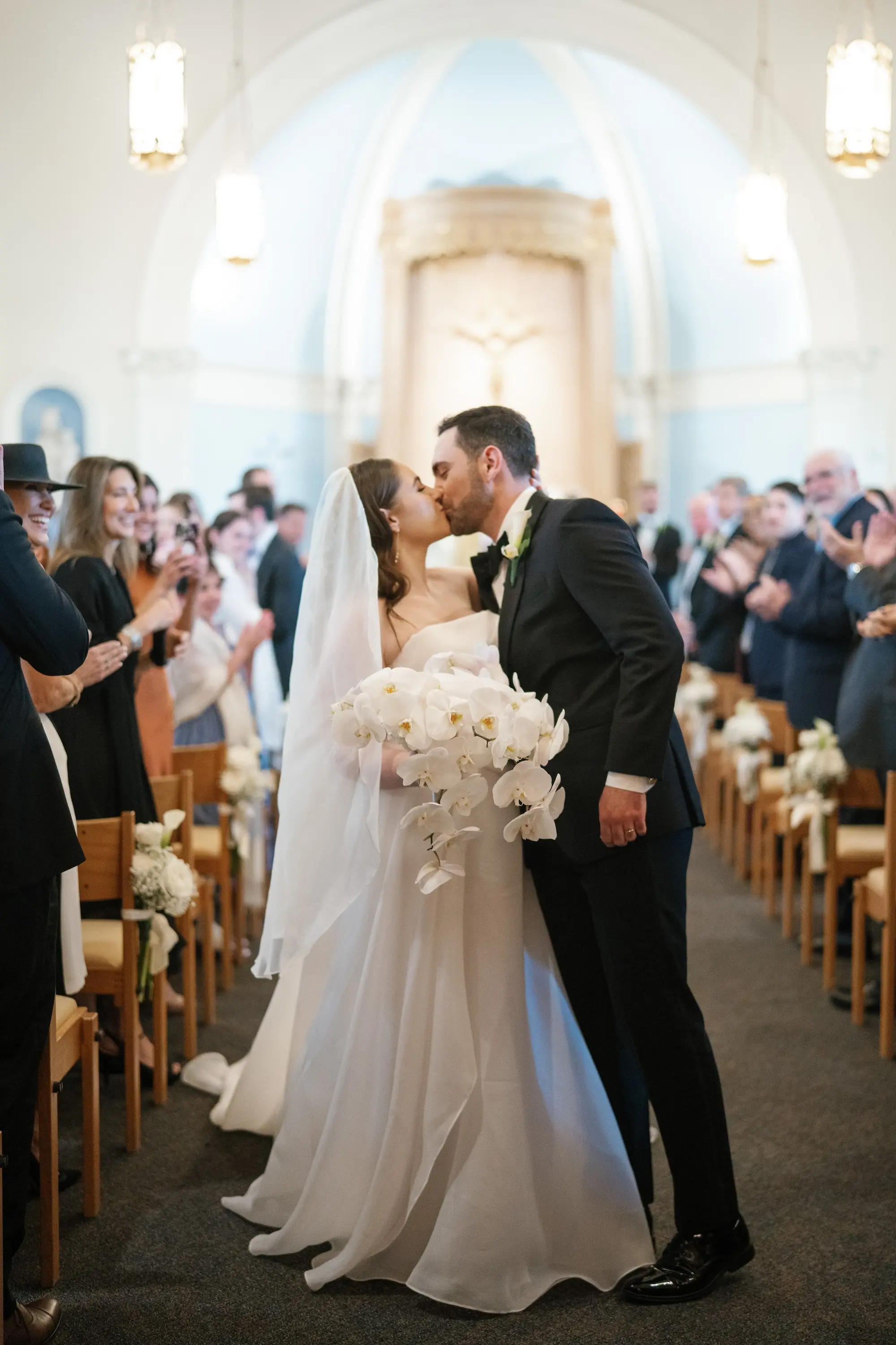 Bride and Groom Just Married Kissing in Wedding Ceremony Aisle Wedding Portrait | White Orchid Bridal Bouquet Inspiration | Traditional Black and White Groom Tuxedo Ideas | Elegant White Saint Bridal Couture Strapless Wedding Gown Inspiration | Traditional Catholic Church Tampa Bay Wedding Ceremony Academy of Holy Names