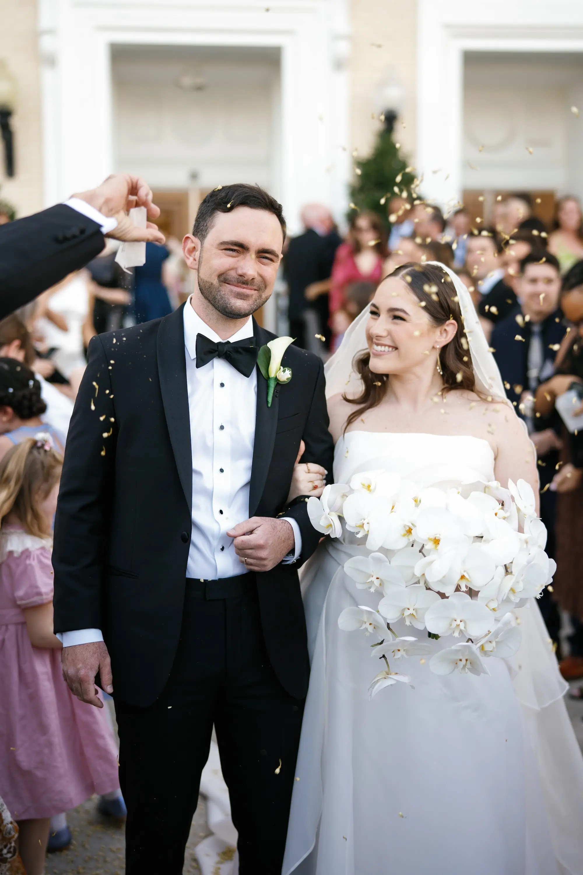 Bride and Groom Flower Petal Wedding Ceremony Exit Wedding Portrait | White Orchid Bridal Bouquet Inspiration | Traditional Black and White Groom Tuxedo Ideas | Elegant White Saint Bridal Couture Strapless Wedding Gown Inspiration