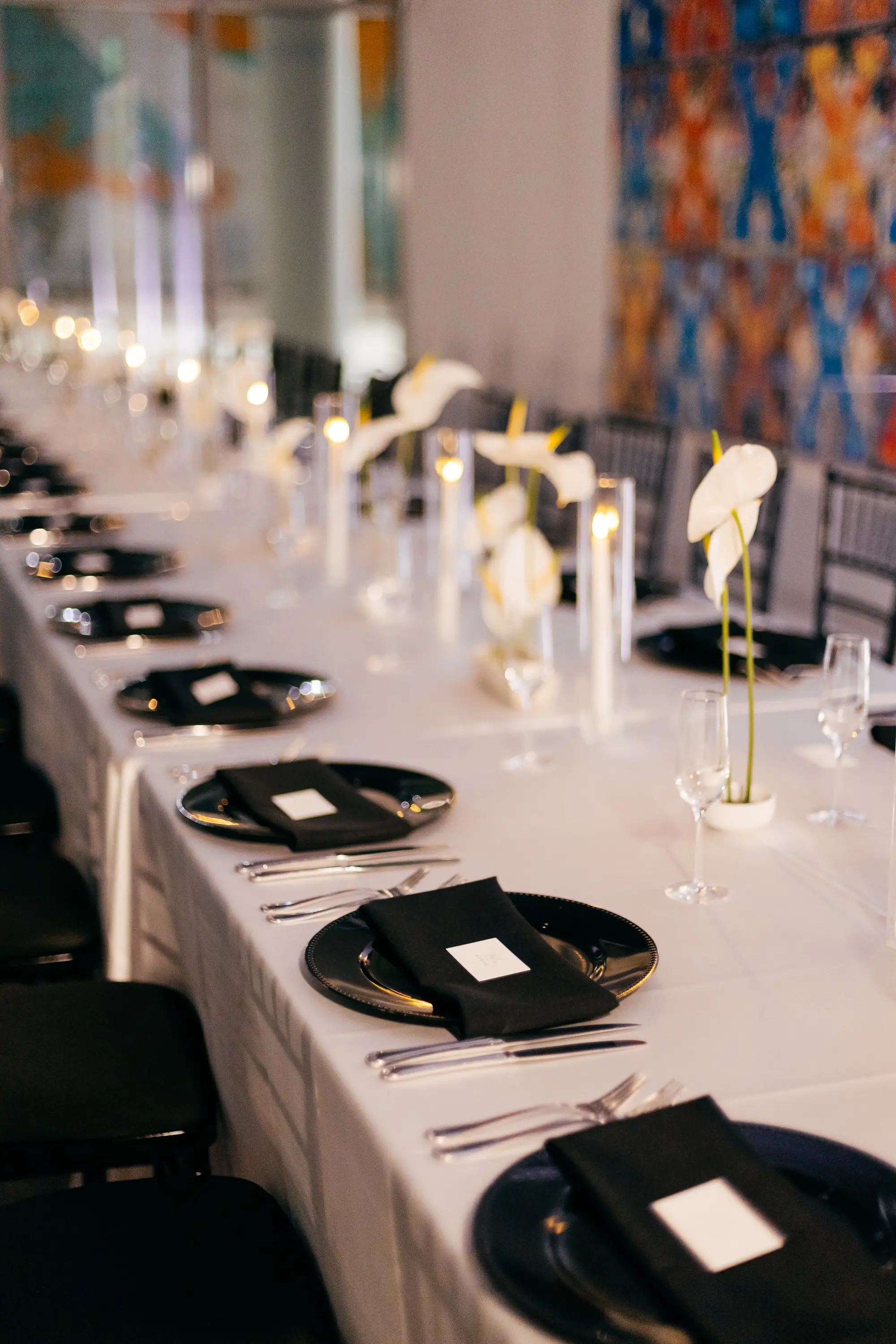 Long Wedding Reception Table with White Linens and Gold Chargers with Black Napkins Tablescape Inspiration | Elegant Modern Black and White Black Tie Wedding Ideas | Single Glass Bud Vases with White Lilies Centerpiece Inspiration | Romantic White Taper Candles in Glass Vases Decor Ideas | Over The Top Rental Linens | Tampa Bay Event Planner Unique Weddings and Events