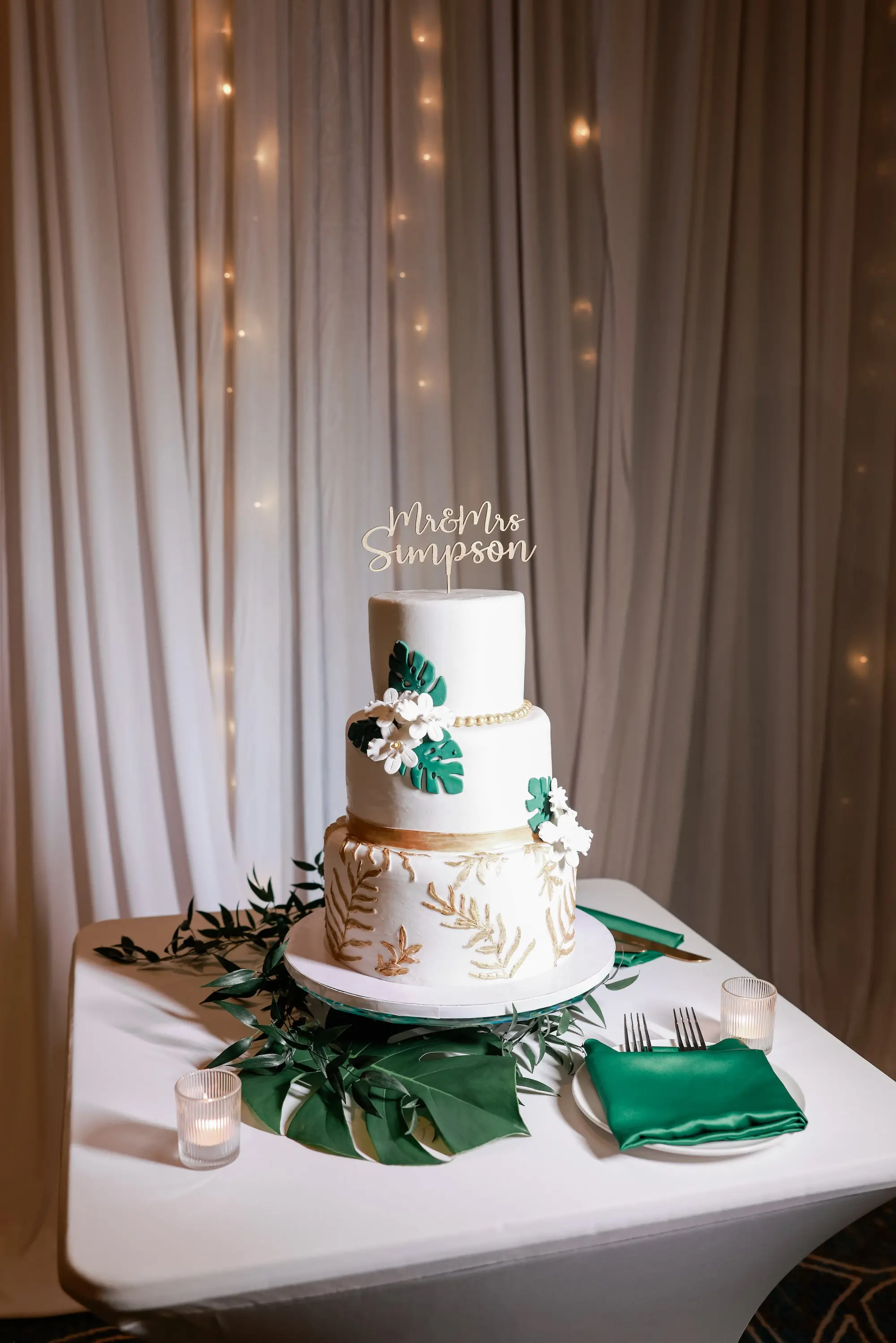 Three Tier White Wedding Cake with Tropical Green and Tan Palm Fronds and White Florals Ideas | Green Palm Fronds Tablescape Decor Inspiration | White Linens with Green Satin Napkins Ideas