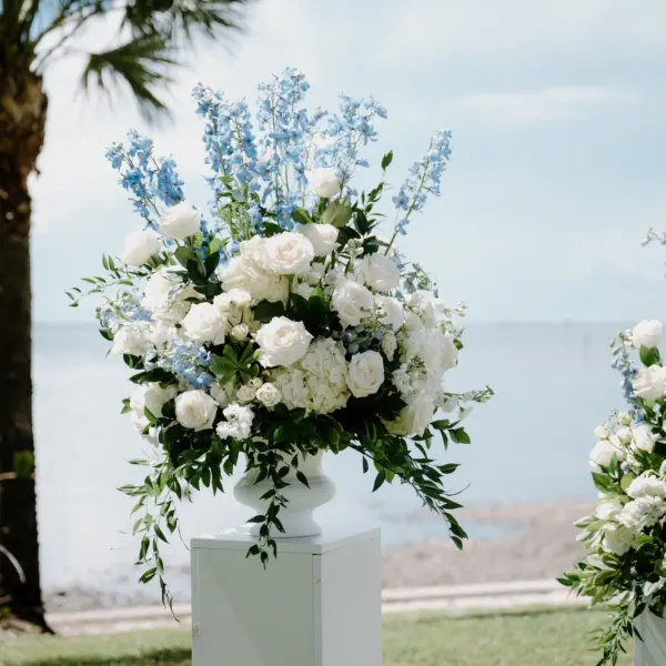 Timeless Wedding Decor Ideas | White Roses and Florals with Blue Delphiniums in White Vases on White Pedestals Wedding Ceremony Floral Arrangement Decor Inspiration | Ocean View Wedding Reception Ideas | Sarasota Florist Beneva Flowers