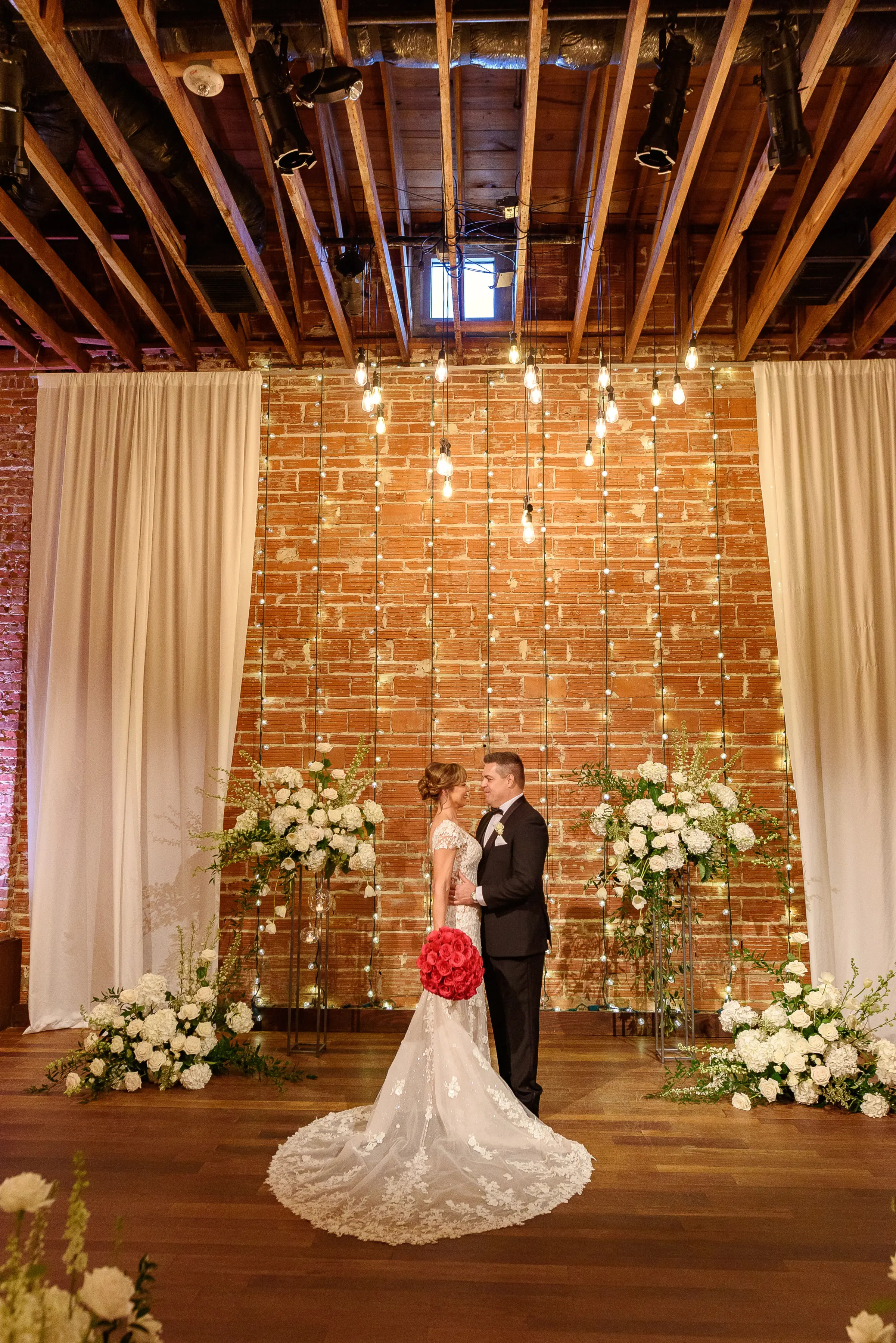 Bride and Groom Wedding Ceremony Portrait | Bright Pink Roses Bridal Bouquet Inspiration | Glamorous White Florals and Greenery Wedding Ceremony Decor Inspiration | Exposed Industrial Brick Wedding Ceremony Venue Ideas | White Ceremony Chairs Inspiration | St. Petersburg Wedding Venue Nova 535 | Tampa Bay Florist Bruce Wayne Florals