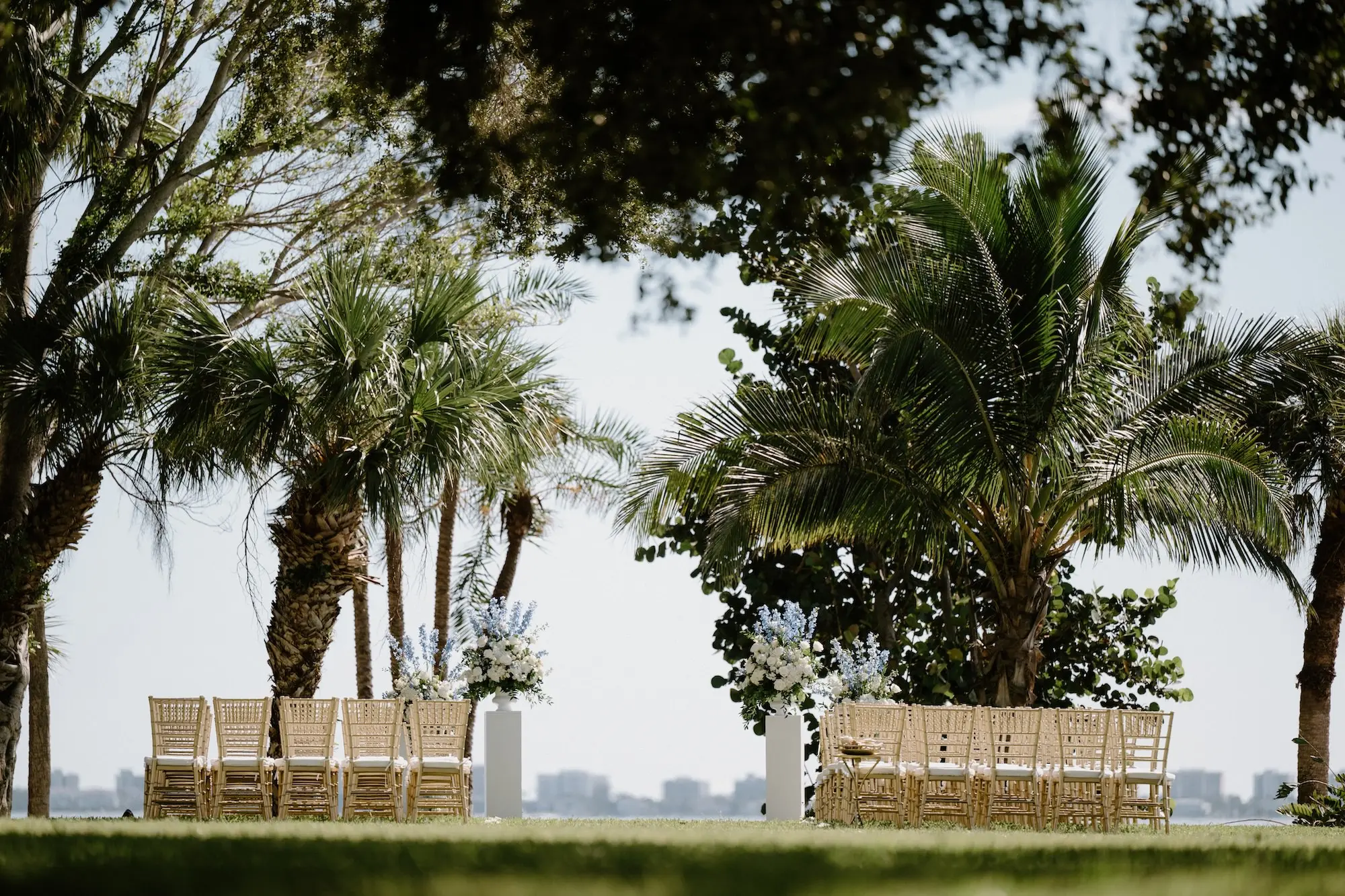 Timeless Wedding Decor Ideas | White Roses and Florals with Blue Delphiniums in White Vases on White Pedestals Wedding Ceremony Floral Arrangement Decor Inspiration | Ocean View Wedding Reception Ideas | Gold Chiavari Ceremony Chairs Inspiration | Sarasota Florist Beneva Flowers