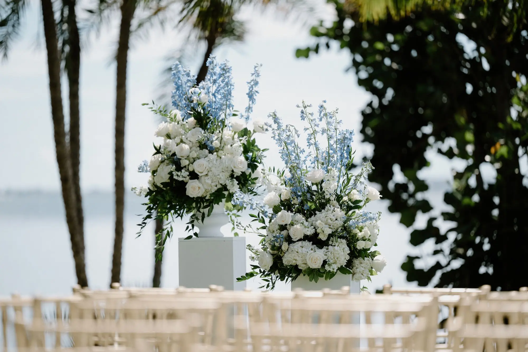 Timeless Wedding Decor Ideas | White Roses and Florals with Blue Delphiniums in White Vases on White Pedestals Wedding Ceremony Floral Arrangement Decor Inspiration | Ocean View Wedding Reception Ideas | Gold Chiavari Ceremony Chairs Inspiration | Sarasota Florist Beneva Flowers