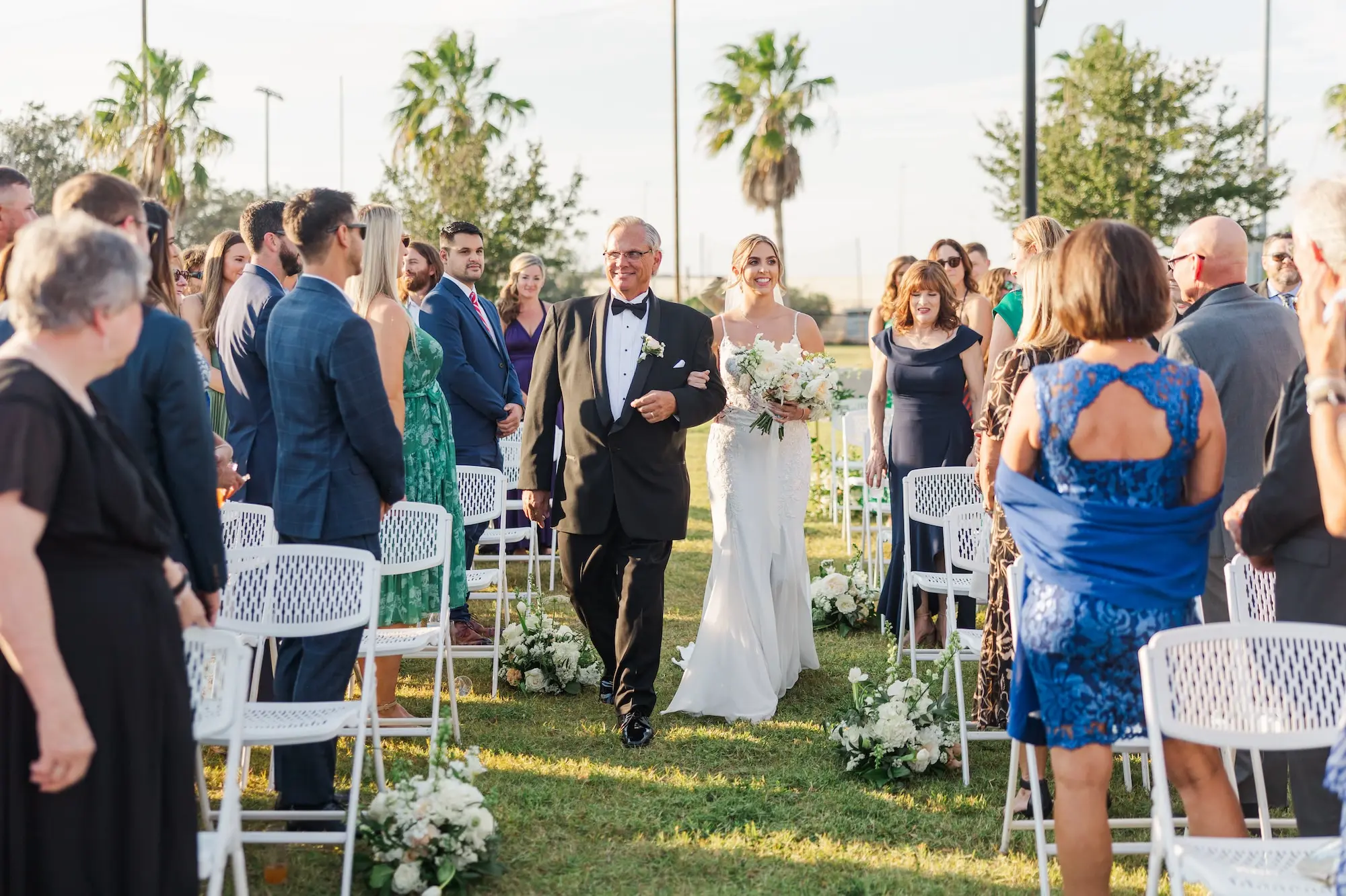 22Classic Emerald Green and Champagne Wedding Inspiration - Classic Emerald Green Downtown Tampa Wedding | Bob Buckhorn Center Bride and Father Walking Down Wedding Ceremony Aisle | Classic White Florals and Greenery Flower Arrangement Aisle Decor Inspiration | White Ceremony Chairs | Florida Photographer Mary Anna Photography | Venue Tampa River Center