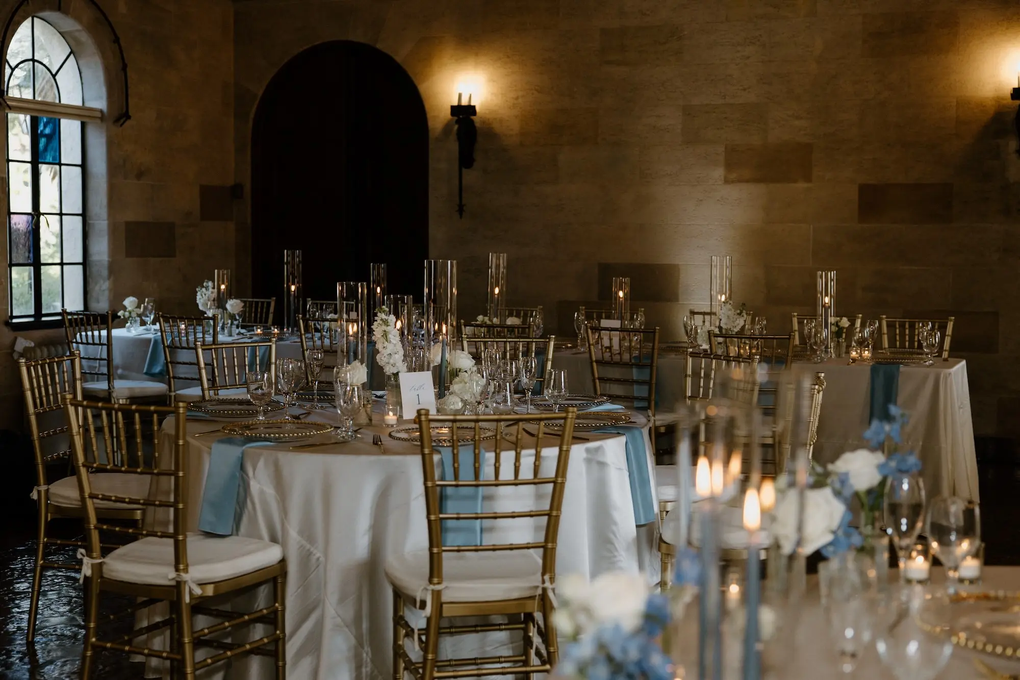 Classic Ballroom Wedding Reception | Bud Vase Centerpiece White Roses and Orchid Flower Arrangement Ideas | Gold Chiavari Reception Chairs | Blue Taper Candles in Glass Vases Wedding Reception Tablescape Decor Inspiration | Clear Chargers with Gold Rims on Blue Satin Napkins Reception Decor Ideas | Sarasota Florist Beneva Flowers