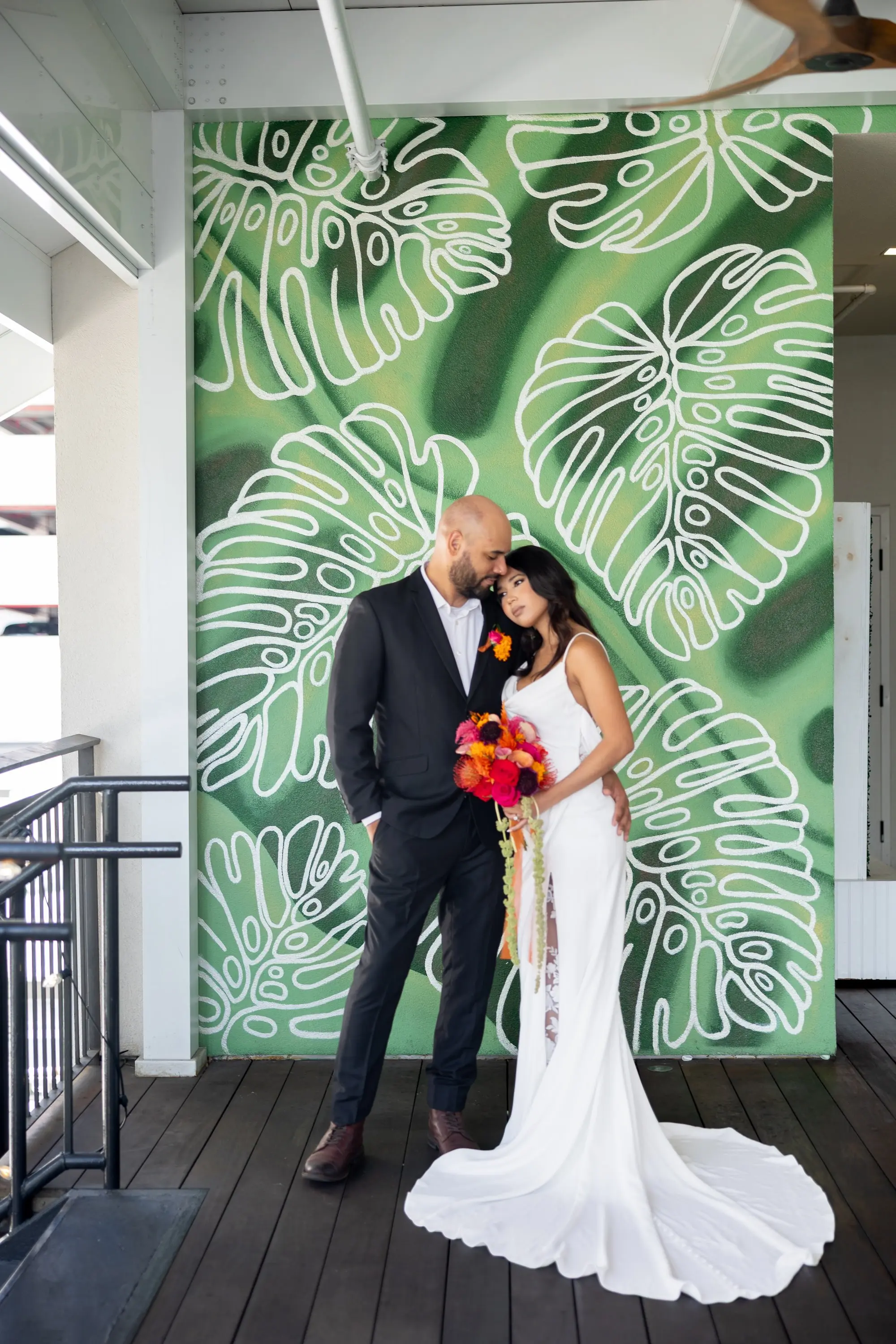 22Vibrant Southwestern Terracotta Pink and Orange Wedding Ideas - Vibrant, Rooftop Wedding Inspiration Shoot | Red Mesa Events Bride and Groom in Front of Green Palm Accent Wall Wedding Reception Portrait | Vibrant Southwest Mexican Wedding Reception Ideas | Bright Pink, Orange, Rust Red, Floral Bridal Bouquet Inspiration | White Fitted, Fit and Flare Wedding Gown with Front Slit with Lace Ideas | Soft Curled Hair with Natural Glam Makeup Inspiration | Tampa Bay Florist Save The Date Florida | St Pete Event Planner Coastal Coordinating | Tampa Bay Photographer Pine and Forge Photography | Downtown St Pete Event Venue Red Mesa Events | Tampa Bay Boutique Truly Forever Bridal | Sarasota Hair and Makeup Artist Femme Akoi Beauty Studio | Content Creator Behind The Vows