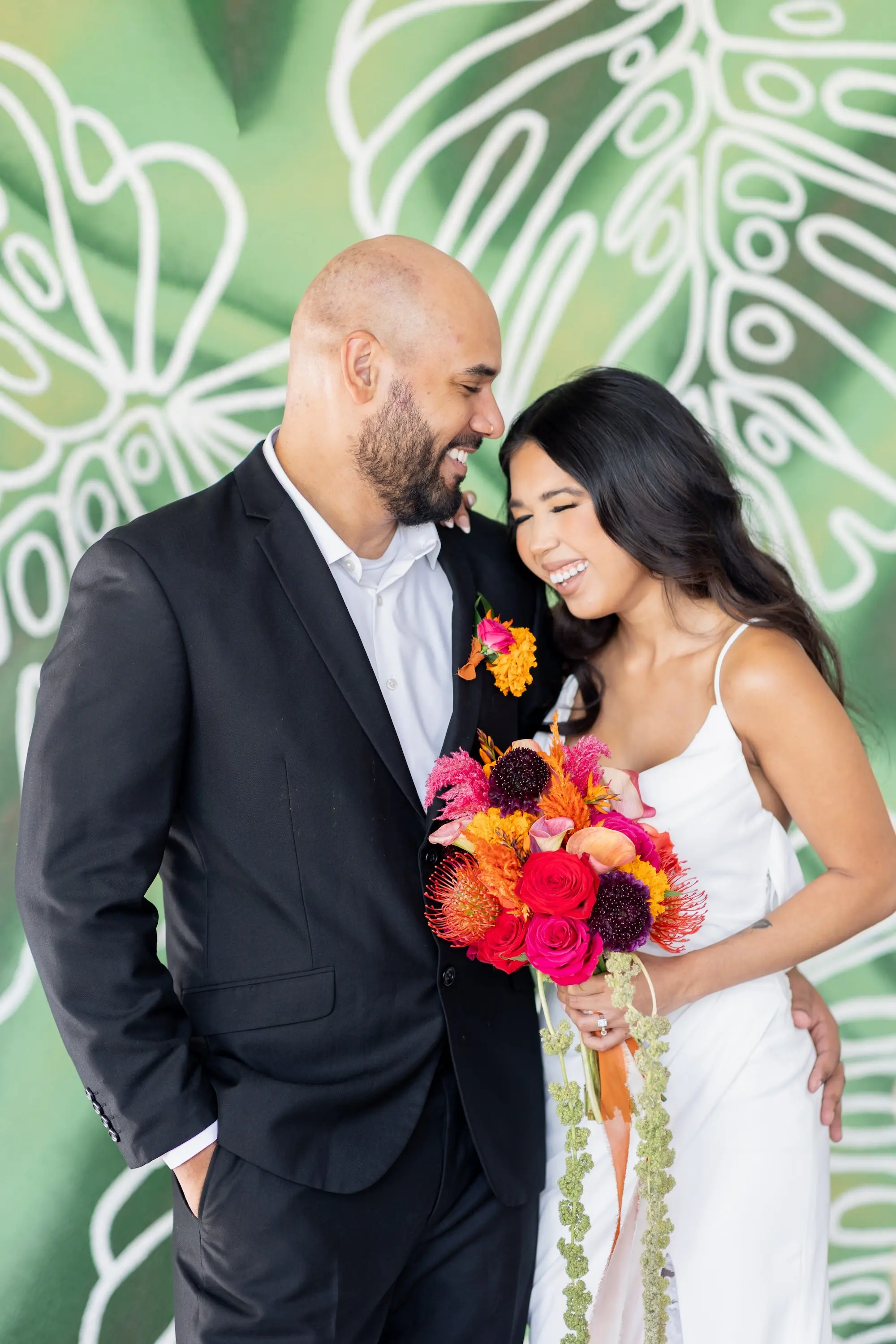 23Vibrant Southwestern Terracotta Pink and Orange Wedding Ideas - Vibrant, Rooftop Wedding Inspiration Shoot | Red Mesa Events Bride and Groom in Front of Green Palm Accent Wall Wedding Reception Portrait | Vibrant Southwest Mexican Wedding Reception Ideas | Bright Pink, Orange, Rust Red, Floral Bridal Bouquet Inspiration | White Fitted, Fit and Flare Wedding Gown with Front Slit with Lace Ideas | Soft Curled Hair with Natural Glam Makeup Inspiration | Tampa Bay Florist Save The Date Florida | Tampa Bay Photographer Pine and Forge Photography | Tampa Bay Boutique Truly Forever Bridal | Sarasota Hair and Makeup Artist Femme Akoi Beauty Studio | Content Creator Behind The Vows