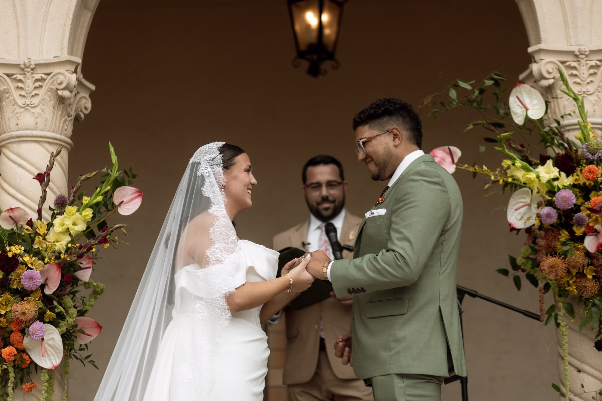 Bride and Groom Wedding Ceremony Vow Exchange Wedding Portrait | White Off the Shoulder Made with Love Wedding Gown Inspiration | Traditional Lace Cathedral Length Wedding Veil Ideas | Green Groom Suit Inspiration | Tropical Fall Colors Yellow, Orange, Purple, Pink, Red Florals with Greenery Wedding Ceremony Altar Decor Inspiration | Sarasota Event Venue Powel Crosley Estate
