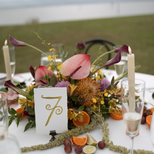 Elegant Fall Colors Tropical Wedding Reception Table Setting Centerpiece Inspiration | Maroon Anthurium Floral Arrangement with Oranges and Grapes Wedding Reception Tablescape Decor Ideas | White and Gold Table Numbers with White Taper Candles Decor Inspiration | Tampa Bay Event Planner The Olive Tree Weddings