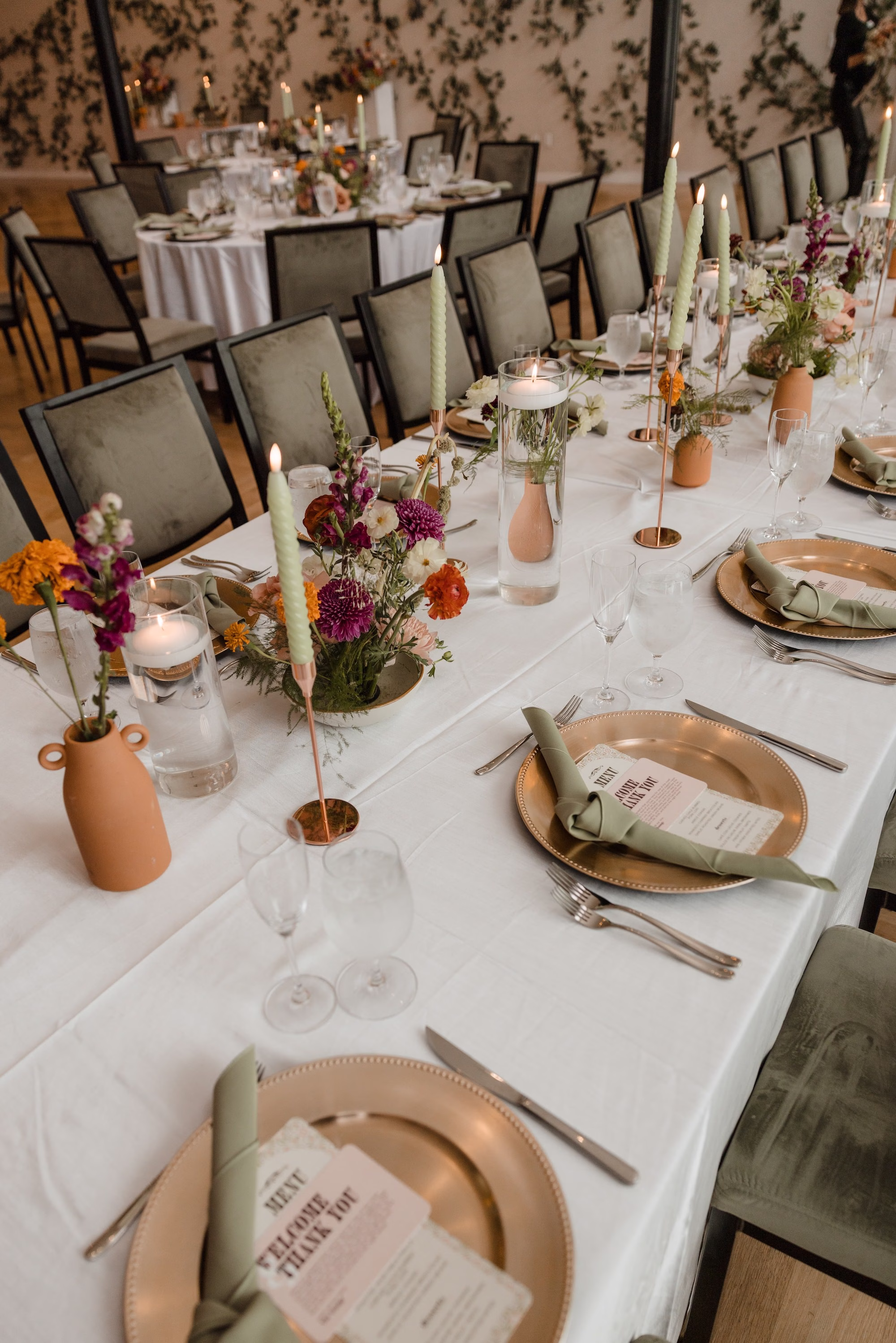 Rich Fall Modern Wedding Reception Table Setting Inspiration | Deep Burgundy Dahlias, Bright Orange Marigolds and Delicate Greenery in Earthy Terracotta Clay Centerpiece Vases Ideas | Taper Candles in Gold Candle Holders Tablescape Decor Inspiration | Gold Chargers with Sage Green Linen Napkins Table Setting Ideas | Ybor City Wedding Venue Hotel Haya