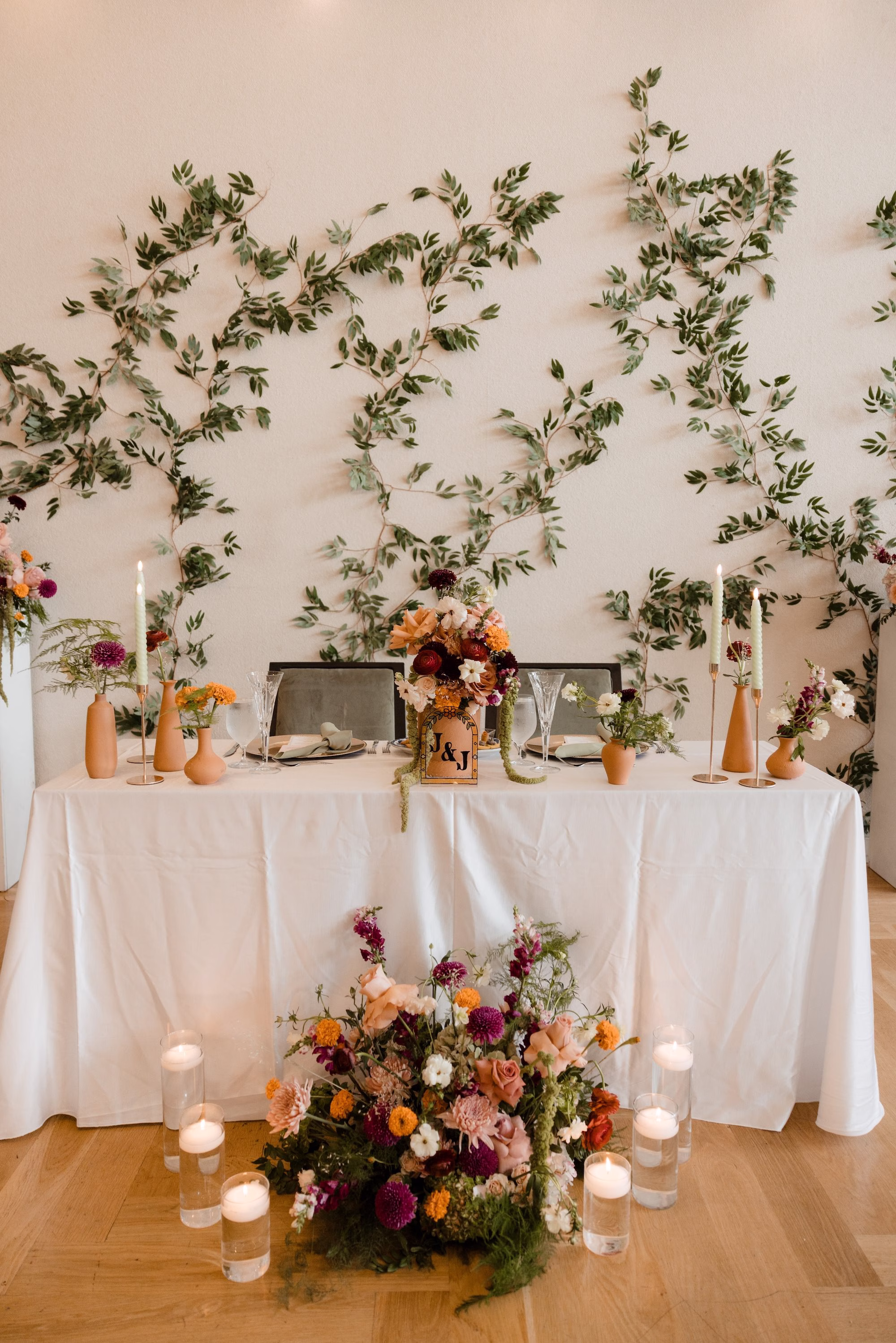 Elegant Urban Ballroom Wedding Reception Sweetheart Table Inspiration | Modern Olive Green and Black Chairs Rich Fall Modern Wedding Reception Table Setting Ideas | Deep Burgundy Dahlias, Bright Orange Marigolds and Delicate Greenery in Earthy Terracotta Clay Centerpiece Vases Ideas | Taper Candles in Gold Candle Holders Tablescape Decor Inspiration | Gold Chargers with Sage Green Linen Napkins Table Setting Ideas | Ybor City Wedding Venue Hotel Haya