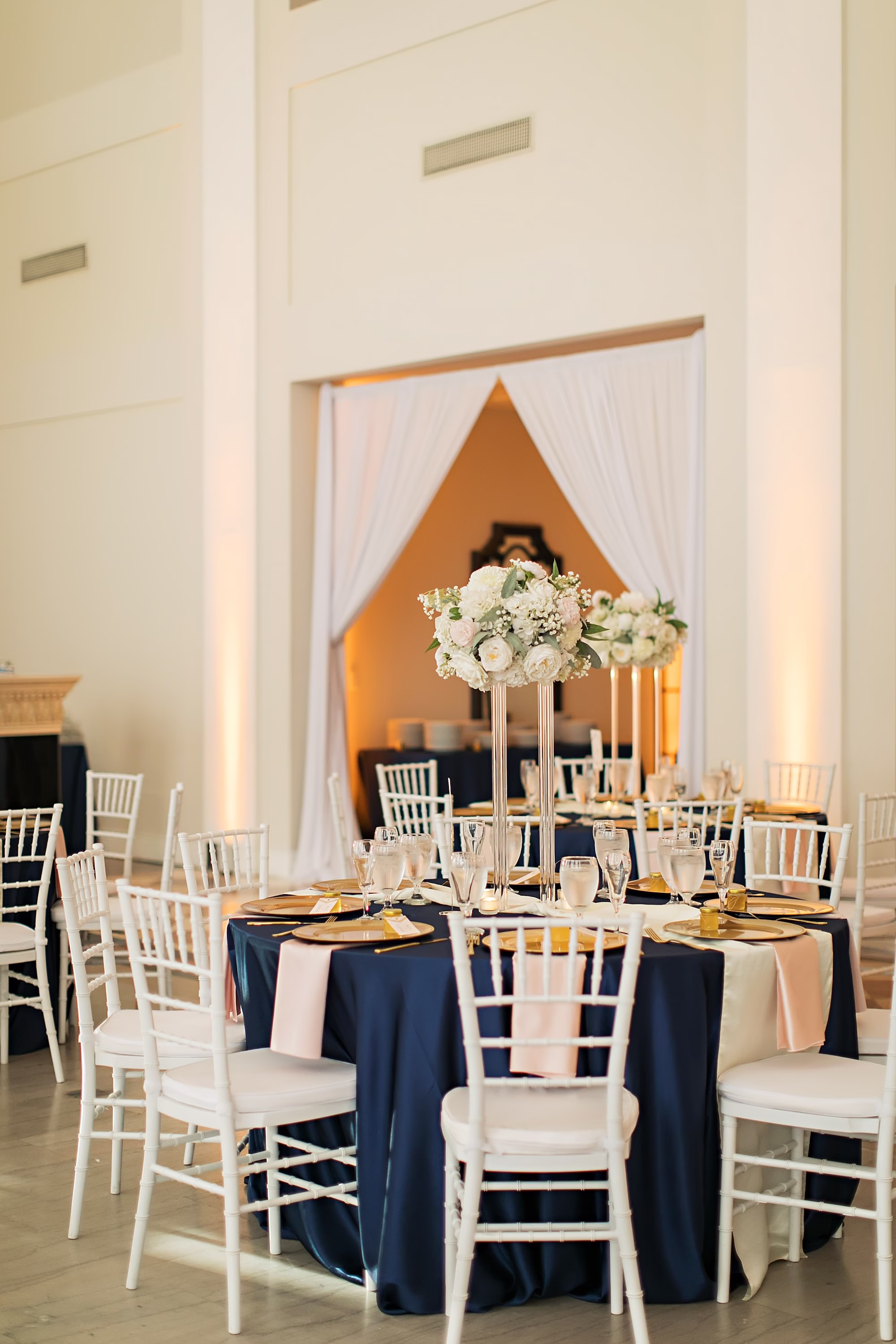 19Elegant Navy Blue and Blush PInk Wedding Ideas - Elegant, Navy and Blush Downtown Tampa Wedding | The Vault Old Glam Navy Blue and Blush Pink Winter Wedding Reception Decor Ideas | Tall White Roses and Baby's Breath Floral Arrangements with Greenery Centerpiece Inspiration | Reception Tables with White Chiavari Chairs Ideas | Navy Blue Linens and Gold Chargers and Satin Blush Napkins Reception Tablescape Decor Inspiration | Downtown Tampa Bay Historic Wedding Venue The Vault