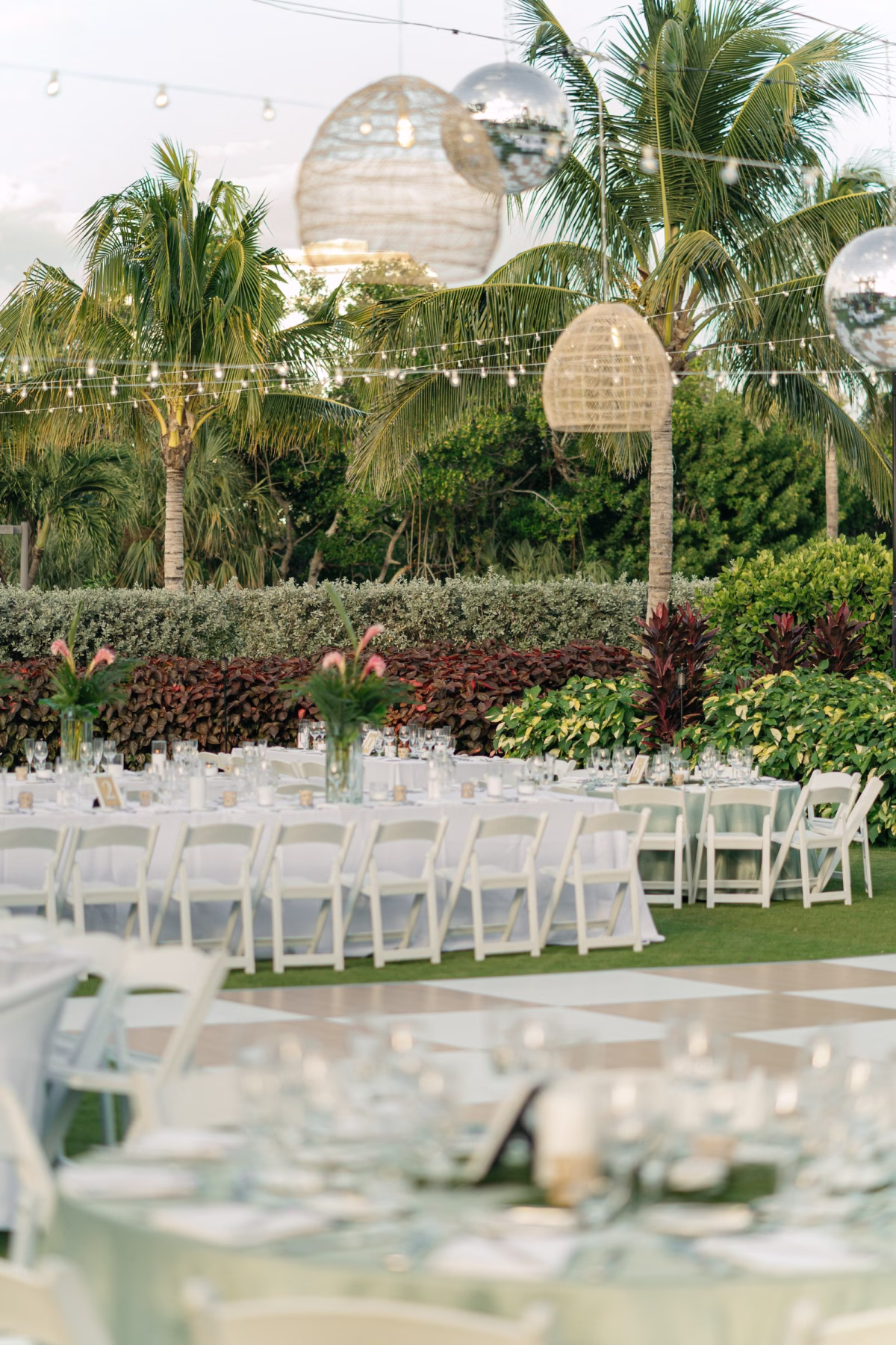 Glamourous Tropical Outdoor Wedding Reception Inspiration | Bistro Lights and Hanging Wicker Baskets Decor Ideas | Long Tables with White Linens and White Chairs Inspiration | Lush White and Green Flower Arrangement Decor Ideas | Tampa Wedding Venue The Resort at Longboat Key Club