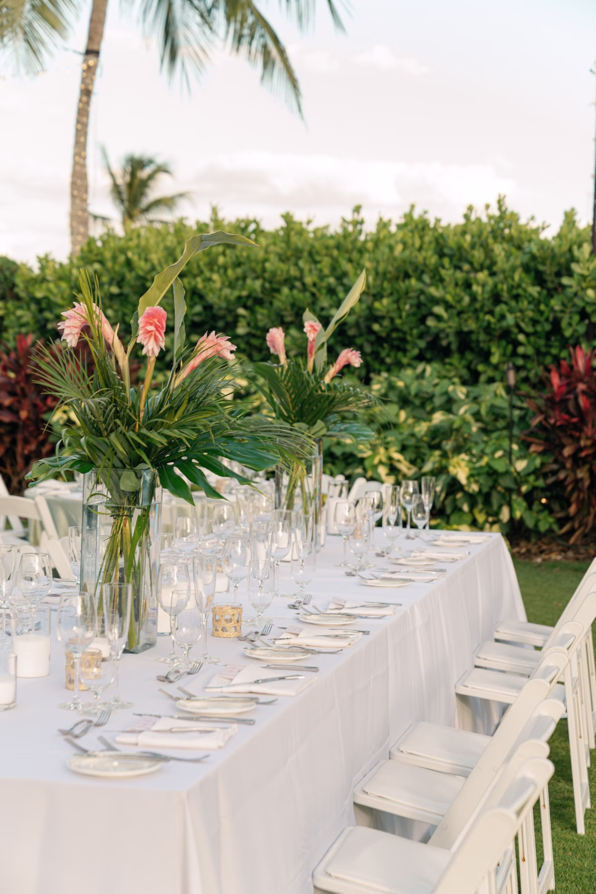 Glamourous Tropical Outdoor Wedding Reception Inspiration | Long Tables with White Linens and White Chairs Ideas | Lush Green Palms with Tropical Red Flowers Floral Arrangement Centerpiece Tablescape Decor Ideas | Tampa Wedding Venue The Resort at Longboat Key Club