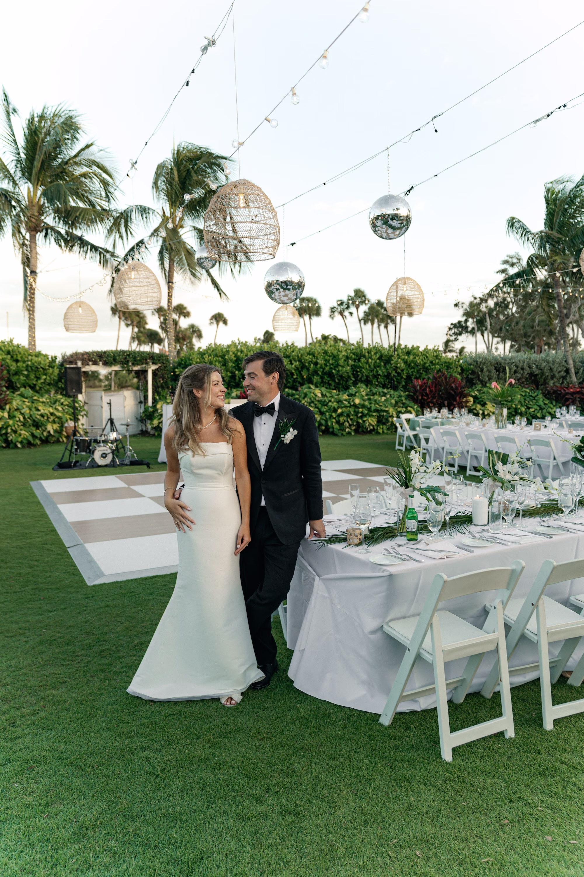 Bride and Groom Wedding Reception Wedding Portrait | Glamourous Tropical Outdoor Wedding Reception Inspiration | Disco Balls and Hanging Wicker Lights Reception Decor Ideas | Long Tables with White Linens and White Chairs Inspiration | Lush White Florals and Green Palm Greenery Centerpiece Flower Arrangement Decor Ideas | Tropical Green Palm Garland Tablescape Decor Inspiration | White and Gold Checkered Dance Floor Ideas | Tampa Wedding Venue The Resort at Longboat Key Club