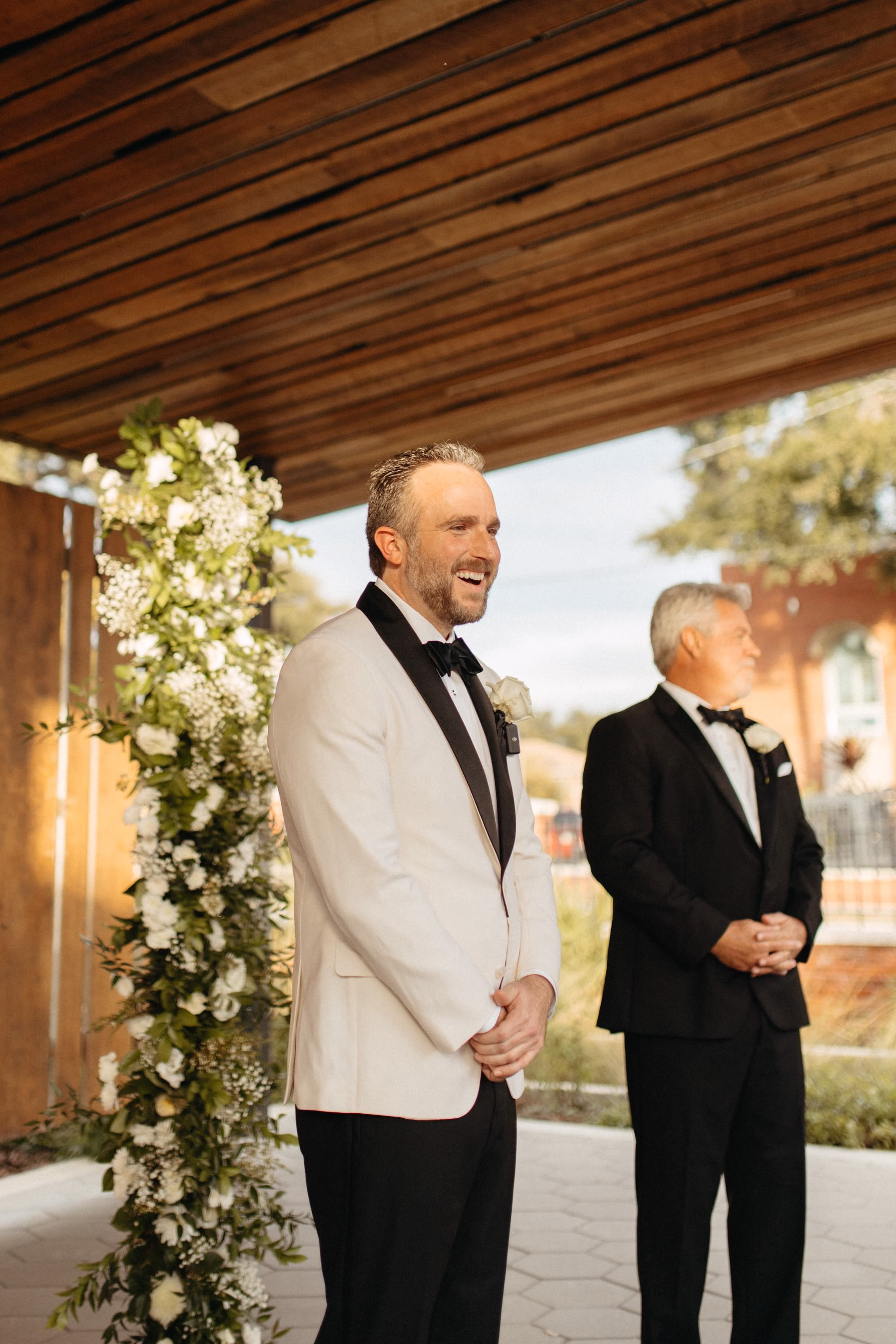 Groom's Reaction to Bride Walking Down Wedding Ceremony Aisle | White Roses and Baby's Breath in Greenery Floral Column Altar Wedding Ceremony Decor Inspiration | Clearwater Florist Lemon Drops Wedding and Events