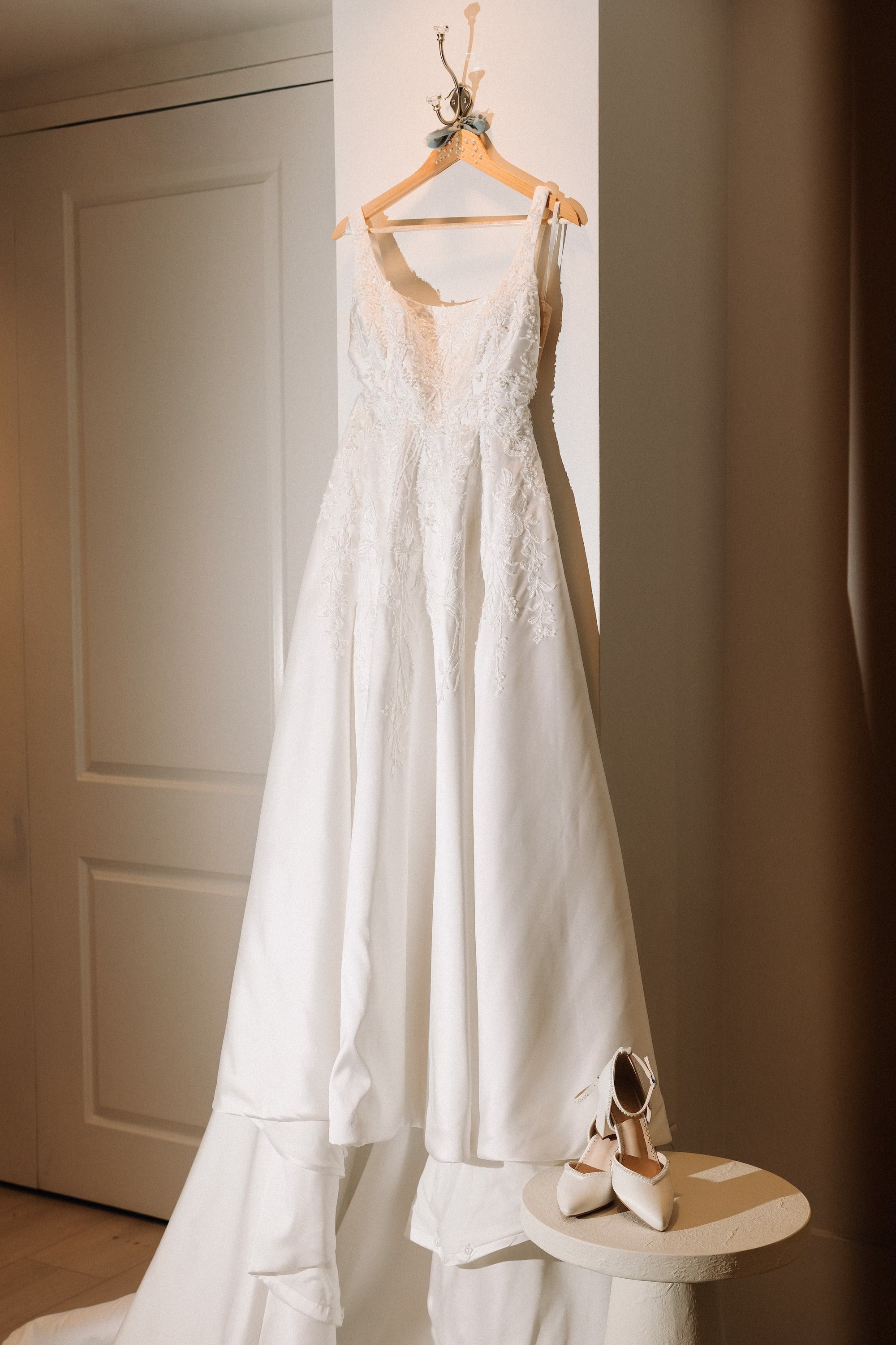 4Coastal Blue and White Rooftop Florida Wedding Ideas - Romantic Blue Coastal St. Pete Beach Wedding | The Hotel Zamora Elegant White Magnolia White A-Line Wedding Gown with Square Neckline and Full Skirt hanging from Wooden Hanger Ideas | White Pearl Bridal Kaliee P Wedding Heels Inspiration