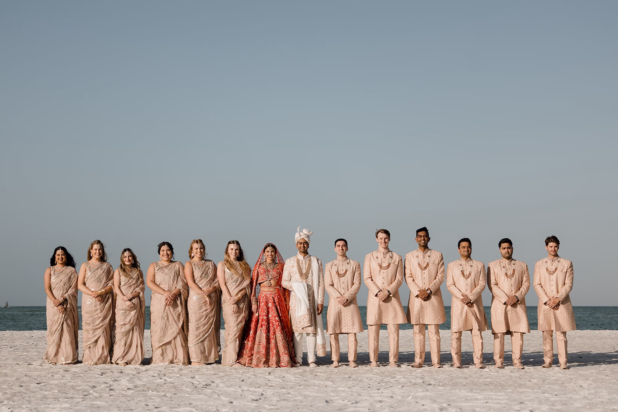 16Tropical Pink and Red Sarasota Beach Indian Wedding Ceremony - Vibrant Pink and Gold Multicultural Sarasota Wedding | Powel Crosley Estate Bride and Groom with Bridal Party on Sarasota Beach Wedding Portrait | Groom Beaded Off-White Sherwani Inspiration | Bright Red and Gold Bridal Lehenga by Kalighata at Kynah Ideas | Elegant Neutral Traditional Indian Gold Sarees, Lehenga Cholis Bridesmaid Dresses Inspiration | Groomsmen Gold Neutral Sherwanis, Kurta Pajamas with Traditional Mala Necklace Attire Ideas | Photographer Evoke Photo and Film