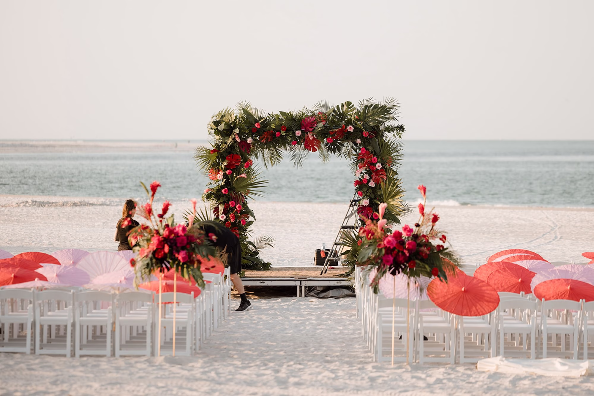 19Tropical Pink and Red Sarasota Beach Indian Wedding Ceremony Venue The Resort at Longboat Key Club - Vibrant Pink and Gold Multicultural Sarasota Wedding | Powel Crosley Estate Beach Oceanfront Wedding Ceremony Inspiration | White Ceremony Chairs with Red and Pink Delicate Umbrellas Parasails Ceremony Favor Ideas | Tropical Floral Rectangular Frame Wedding Ceremony Altar Arch with Lush Palm Frond and Fern Greenery with Vibrant Hot Pink, Red and Orange Florals Inspiration | Sarasota Beach Event Venue The Resort at Longboat Key Club