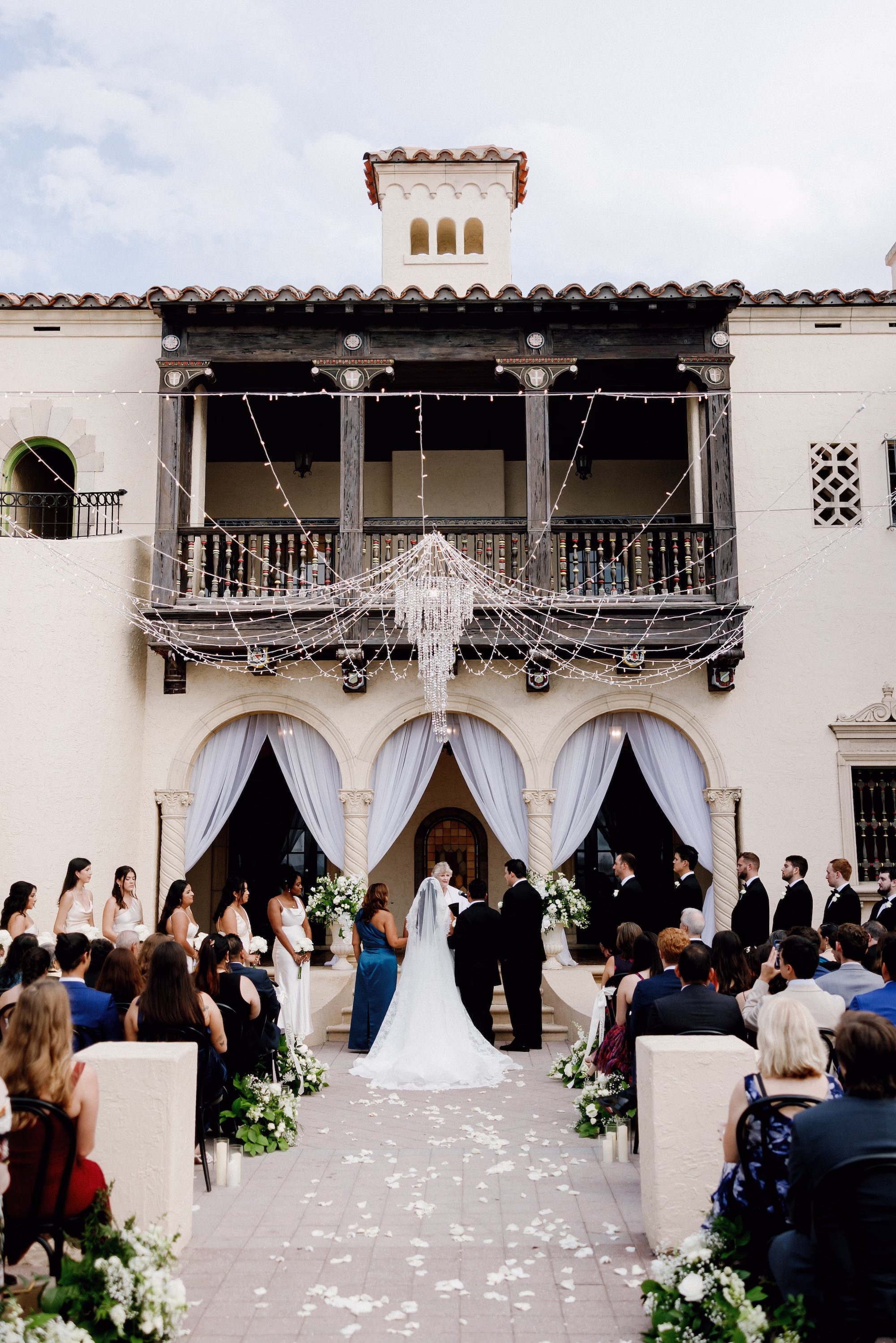 Bride and Groom Wedding Ceremony Vow Exchange Wedding Portrait | Black and White Outdoor Fall Florida Wedding Ceremony Inspiration | Overhead Bistro Lights with Crystal Chandelier Altar Decor Ideas | Black Wedding Ceremony Chairs Inspiration | White Floral Arrangements with Lush Greenery Aisle Decor Ideas | Tampa Florist Save The Date Florida | Sarasota Planner B Eventful | Sarasota Event Venue Powel Crosley Estate