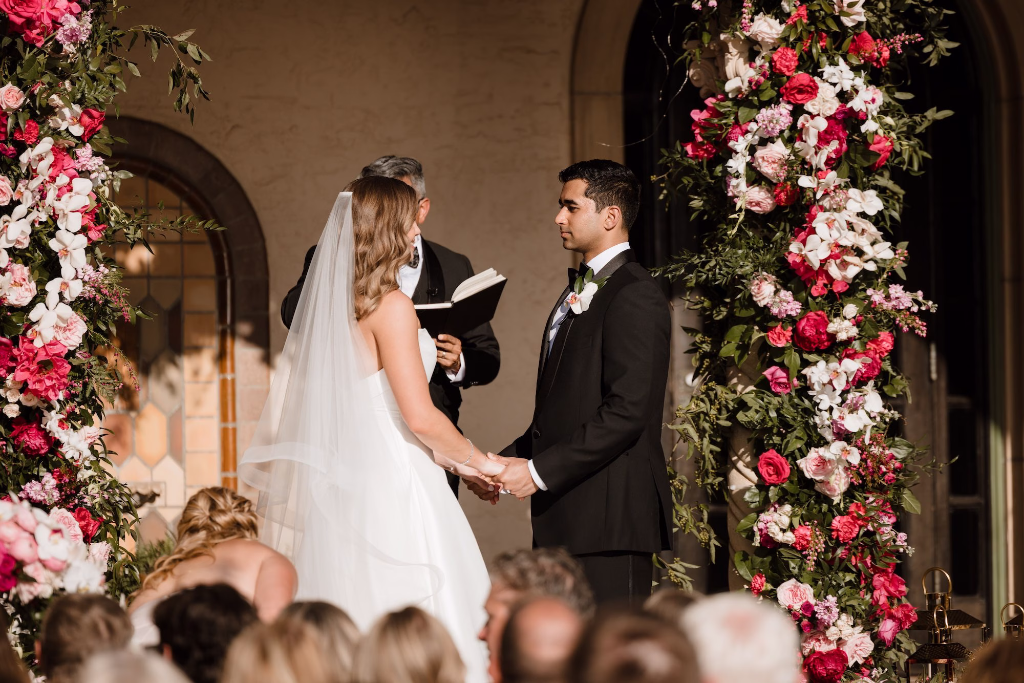 59Romantic Pink and Gold Waterfront Florida Wedding - Vibrant Pink and Gold Multicultural Sarasota Wedding | Powel Crosley Estate Bride and Groom Exchange Wedding Vows Wedding Ceremony Reception Portrait | Strapless White Kelly Faetanini Full Skirt Wedding Gown Inspiration | White Orchid and Red Rose Bridal Bouquet Ideas | Lush Full-Length Floral Arch with Pink, Red and Blush Roses, Hydrangeas and Greenery Decor Inspiration | Tampa Bay Photographer Evoke Photo and Film