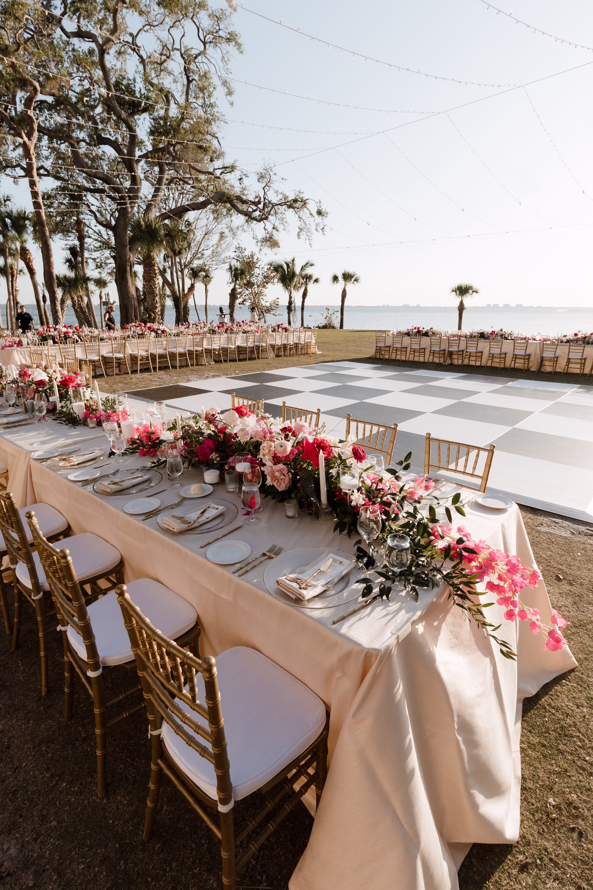 69Romantic Pink and Gold Waterfront Florida Wedding Sarasota Venue Powel Crosley Estate - Vibrant Pink and Gold Multicultural Sarasota Wedding | Powel Crosley Estate Garden Romantic Outdoor Wedding Reception | Lush Long Feasting Table with Pink, Red and Blush Roses, Hydrangeas and Greenery Garland Centerpiece Reception Decor Inspiration | Candlelight Tablescape Decor Ideas | String Lights and Candlelit Table Reception Decor Inspiration | Black and White Checkered Dance Floor Ideas | Sarasota Wedding Venue Powel Crosley Estate
