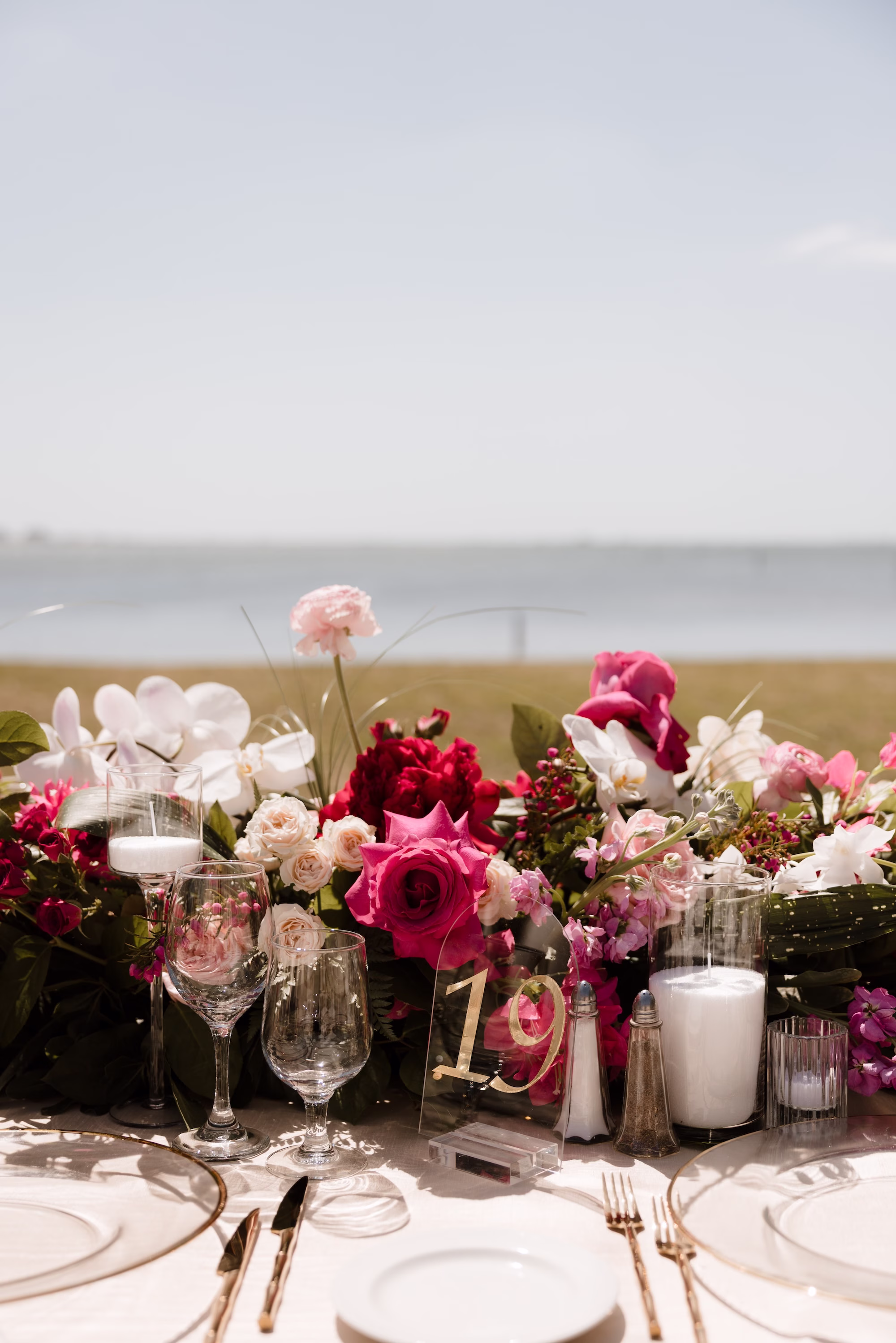 70Romantic Pink and Gold Waterfront Florida Wedding - Vibrant Pink and Gold Multicultural Sarasota Wedding | Powel Crosley Estate Oceanfront Outdoor Wedding Reception Inspiration | Long Feasting Table with Pink, Red and Blush Roses, Hydrangeas and Greenery Garland Centerpiece Reception Decor Inspiration | Acrylic Clear and Gold Table Number Tablescape Decor Ideas